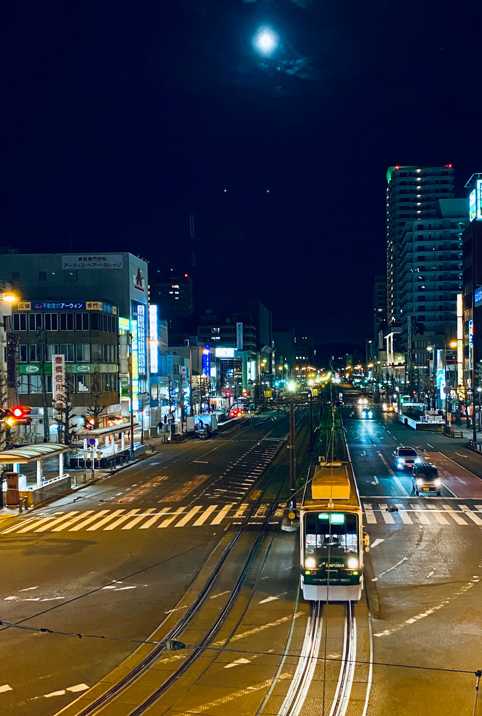 Straßenbahn, die nachts durch eine Stadt unter einem hellen Mond fährt