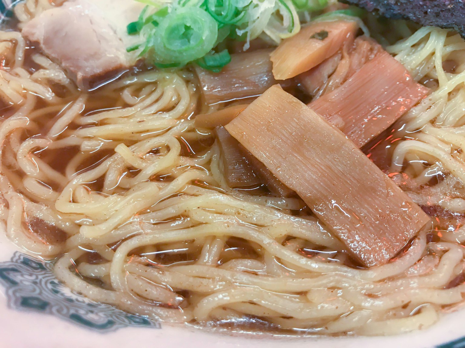 拉面的特写图像，面条、叉烧、竹笋和葱可见