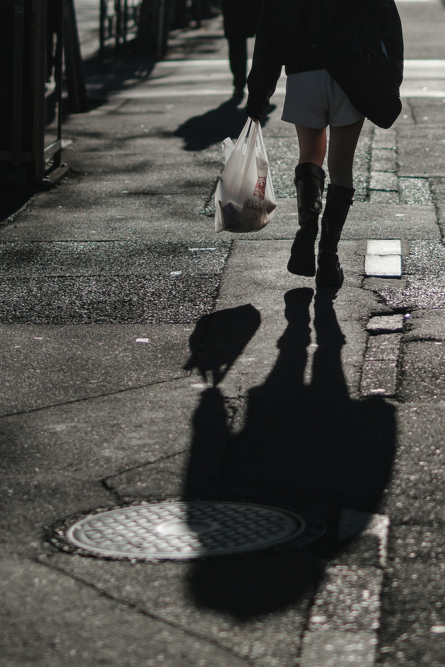 Una persona che cammina per strada con una busta della spesa che proietta un'ombra
