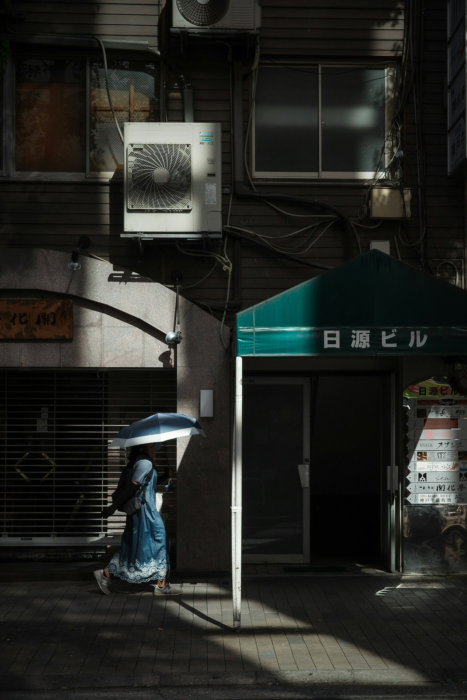 Una donna con un ombrello blu che cammina davanti a un edificio in un angolo di strada buio