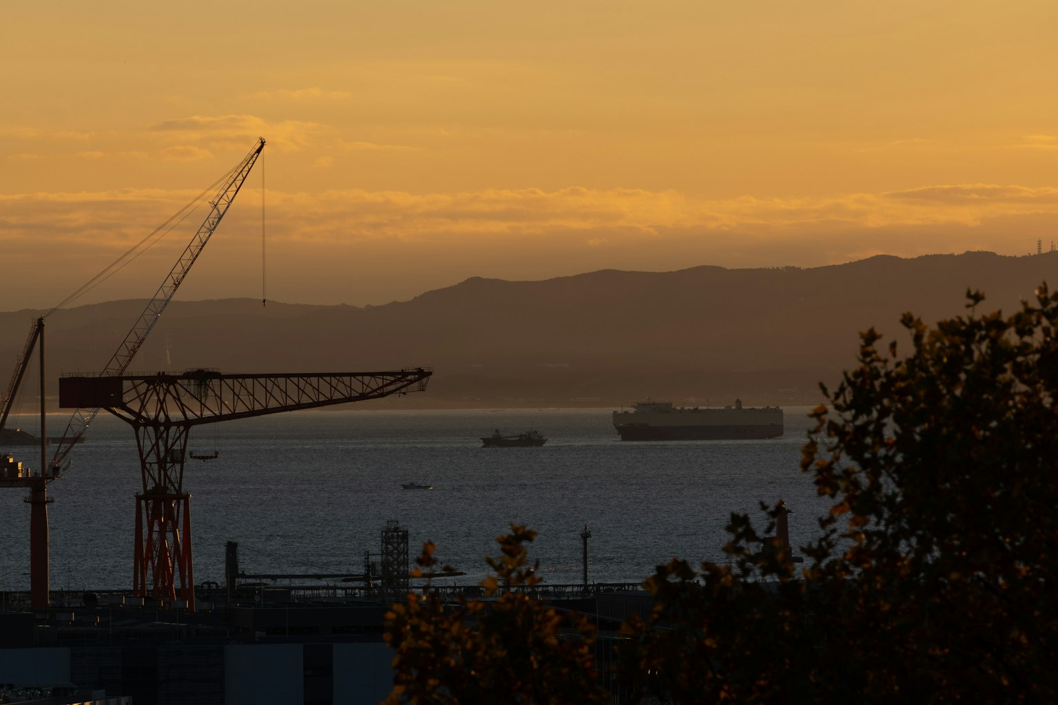 Silueta de una grúa y barcos en el mar durante el atardecer
