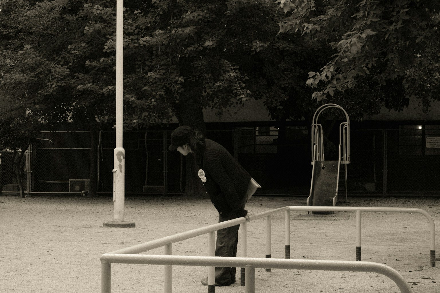 一個人靠在公園的欄杆上，黑白色調，背景有樹木