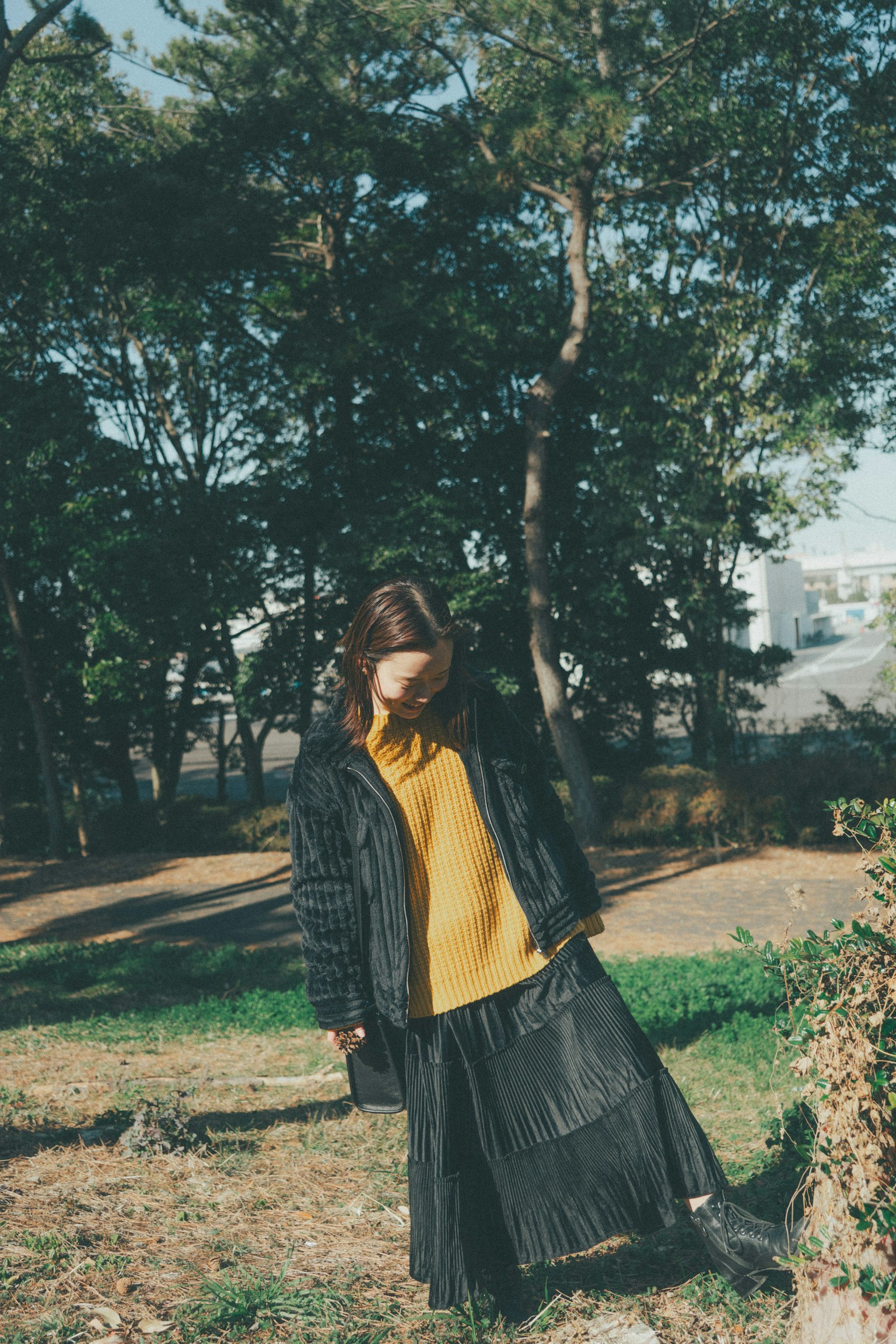 Donna in cappotto nero e maglione giallo in piedi in un parco