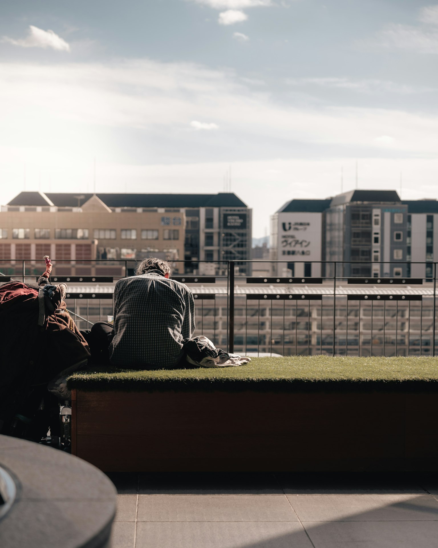 Elderly person sitting on grass in front of modern buildings