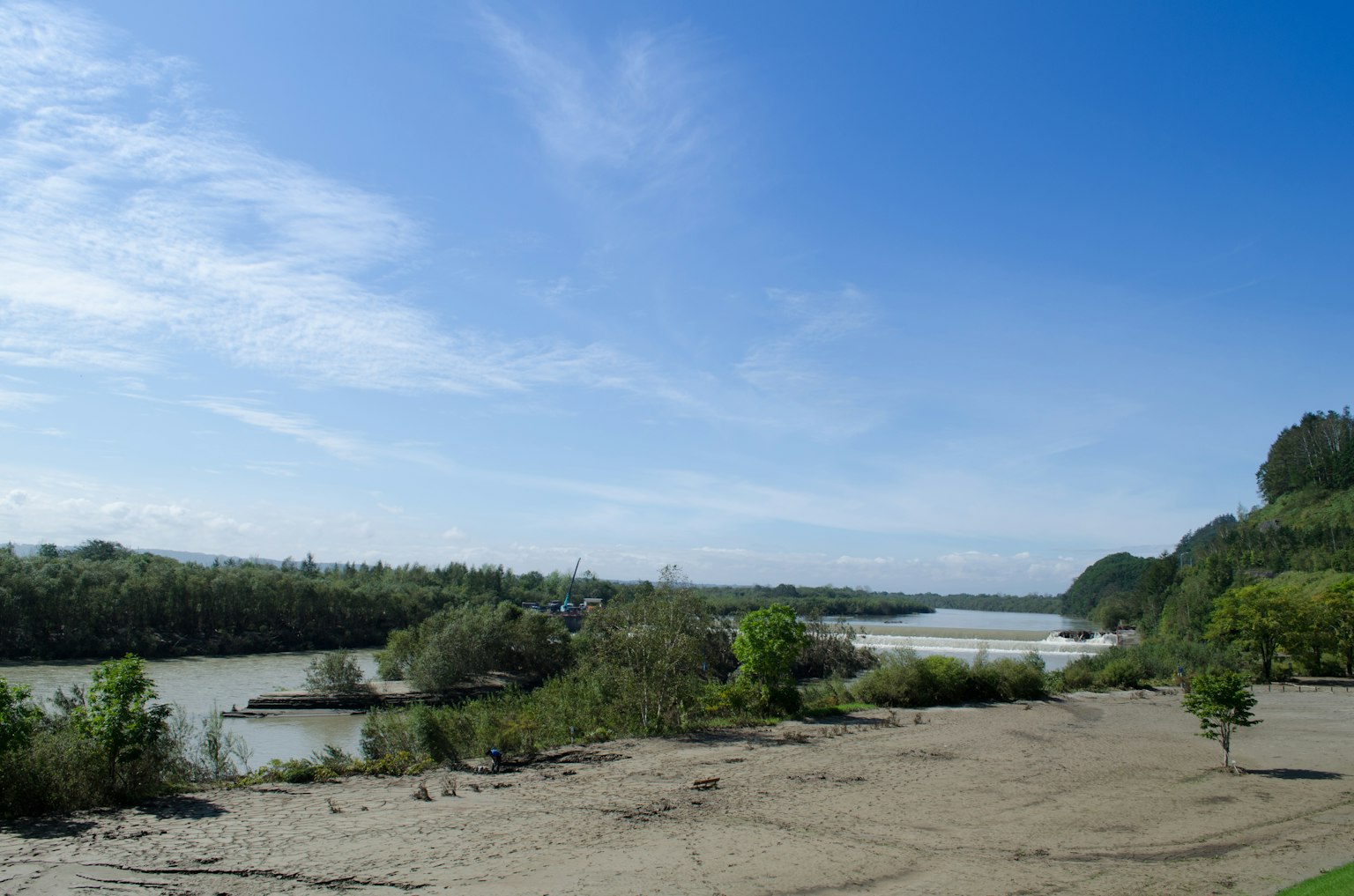 Scenic view of a river under a blue sky with sandy terrain and greenery
