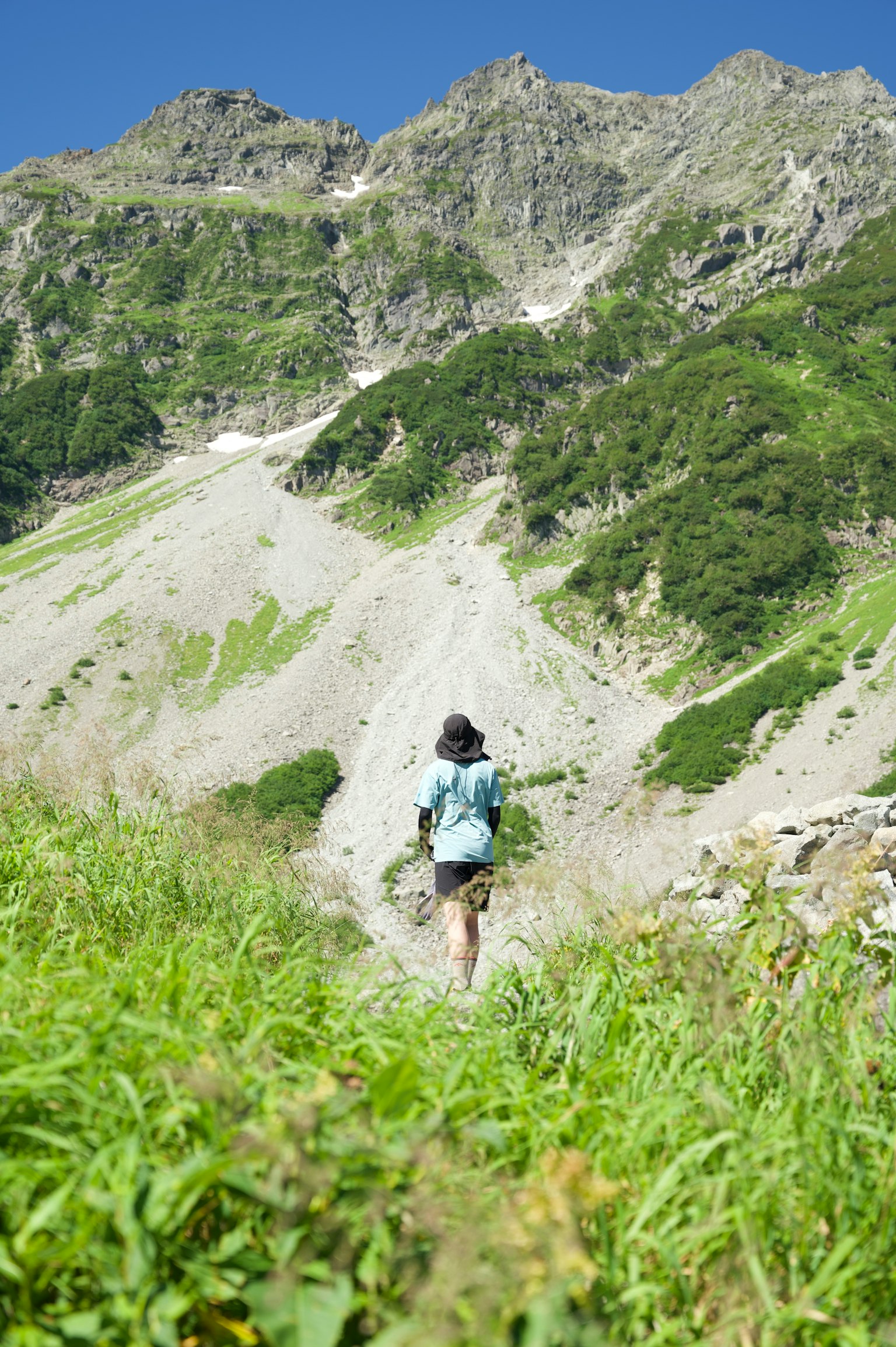 Woman walking on a mountain path with green grass and rocky terrain