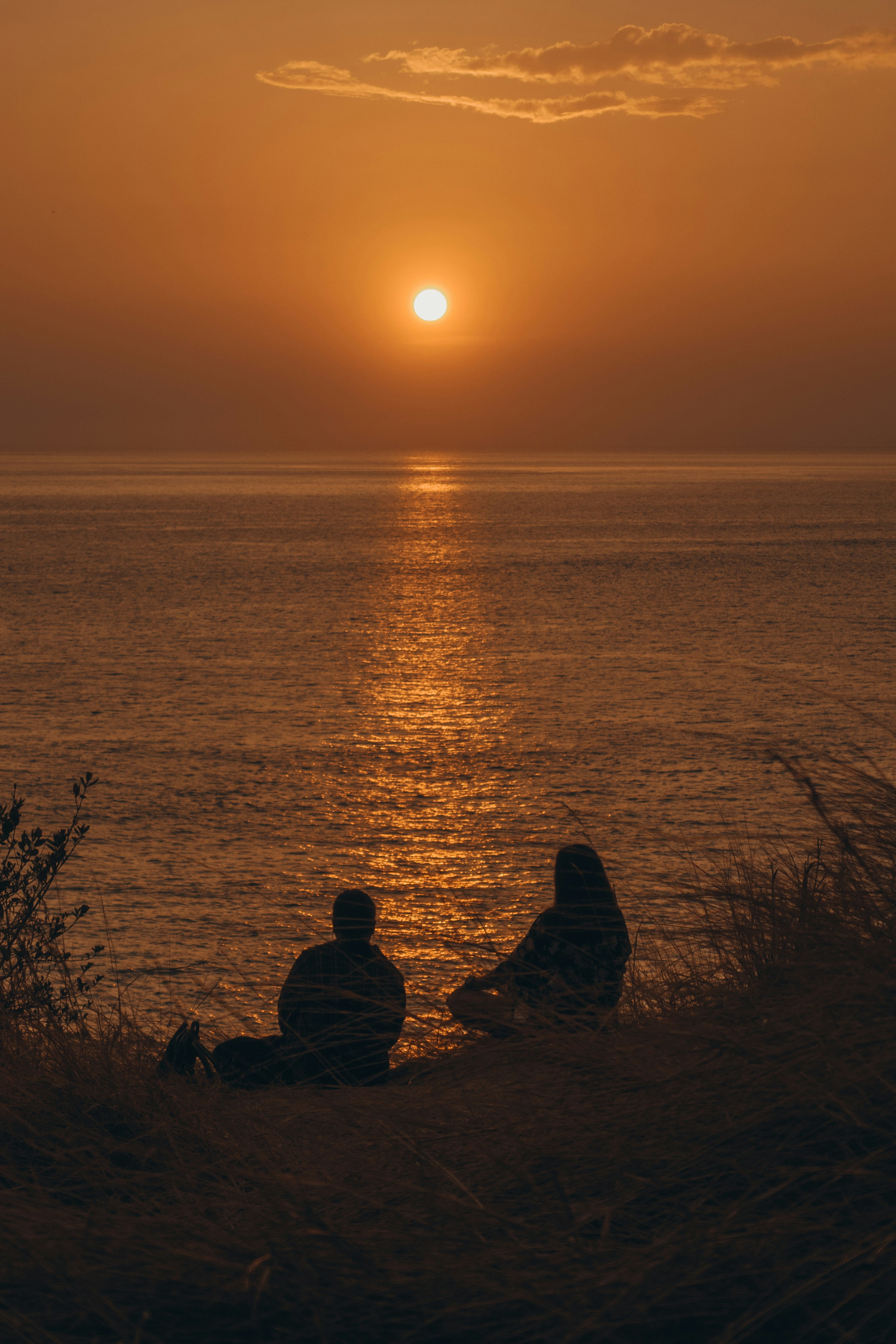 夕日を眺める二人のシルエット 海の上に反射するオレンジ色の光