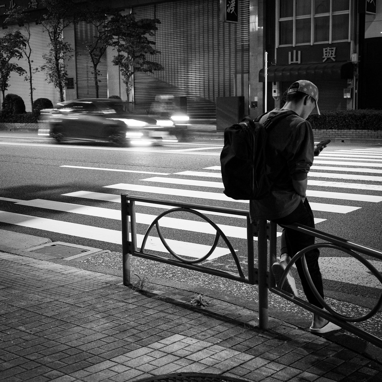 Orang yang melihat smartphone di malam hari di jalan kota dengan garis penyeberangan