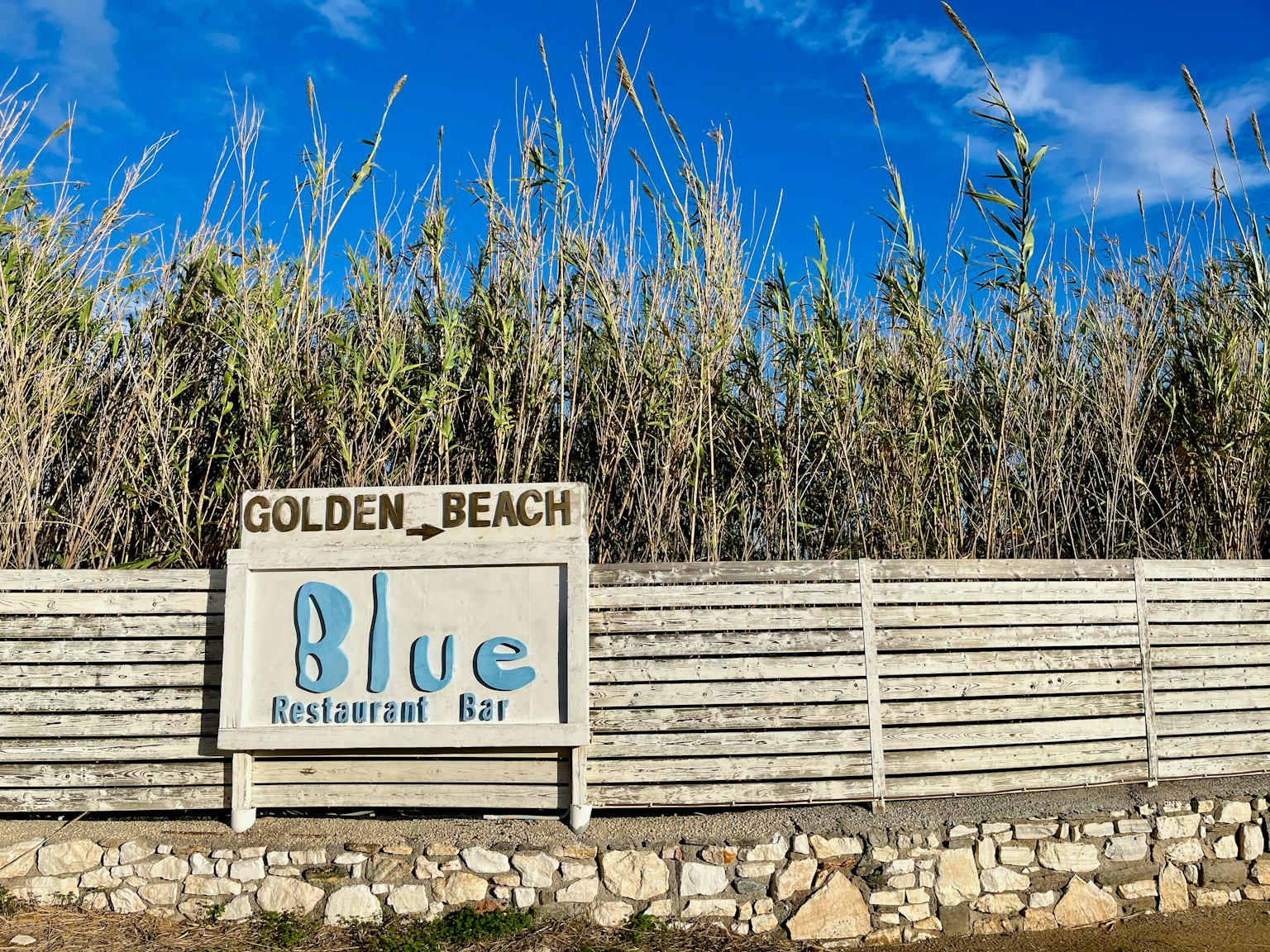 Papan restoran bar Blue di Golden Beach dikelilingi rerumputan tinggi