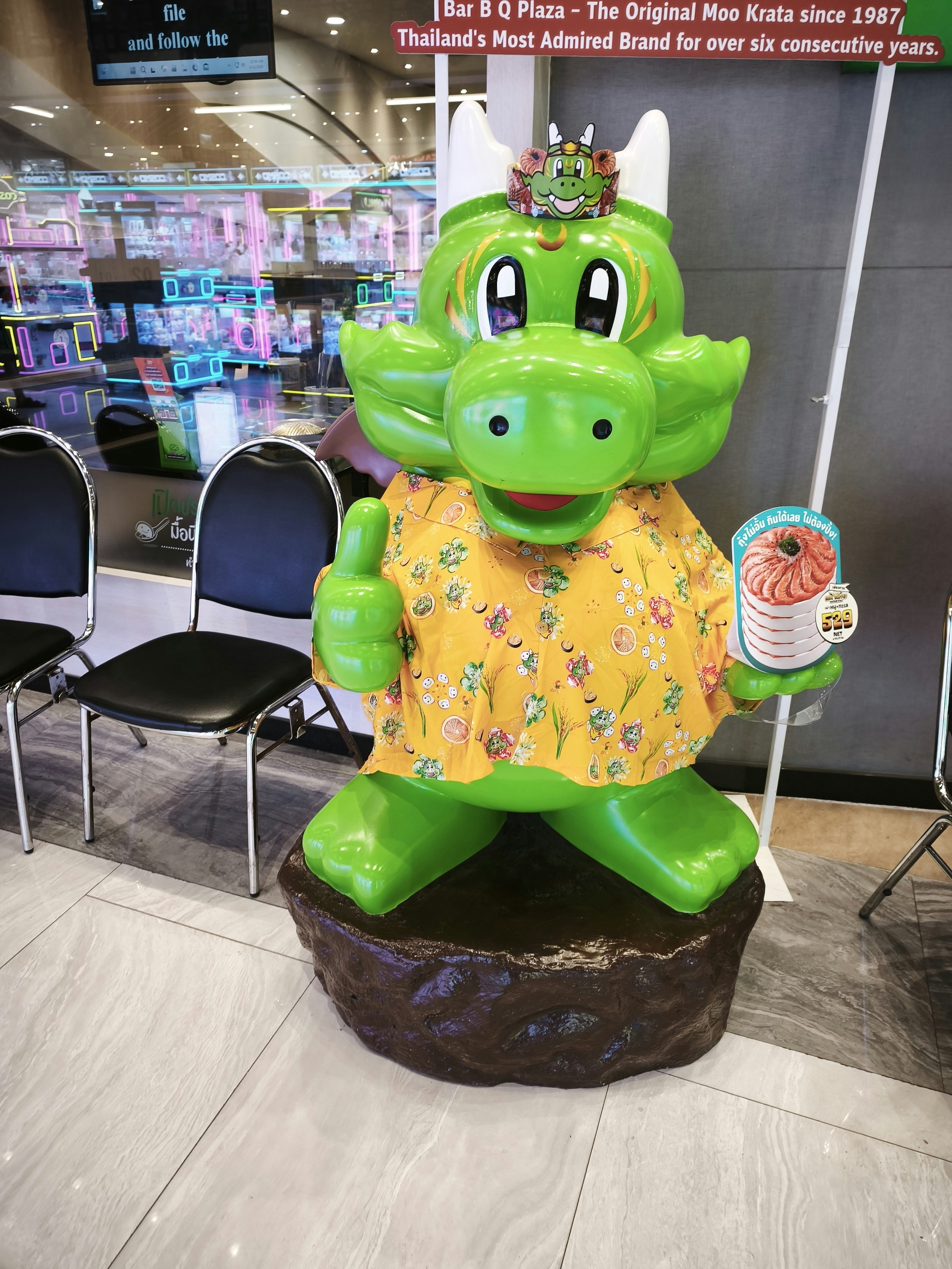 緑の恐竜キャラクターの着ぐるみが店内でポーズ
