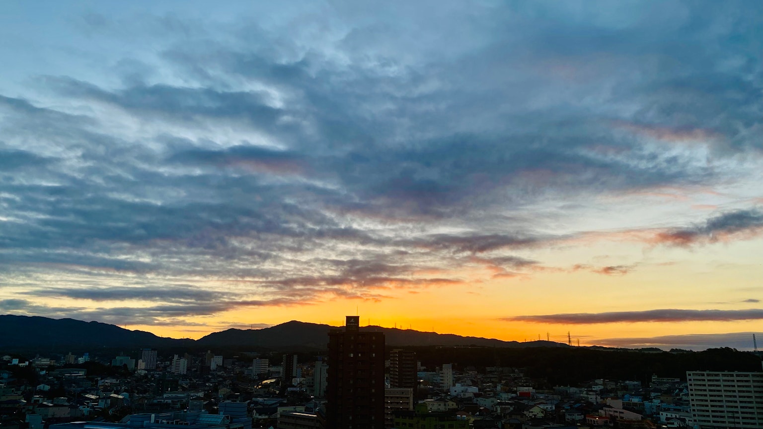 Sonnenuntergangshimmel mit Wolken und Bergsilhouette vor einer Stadtsilhouette