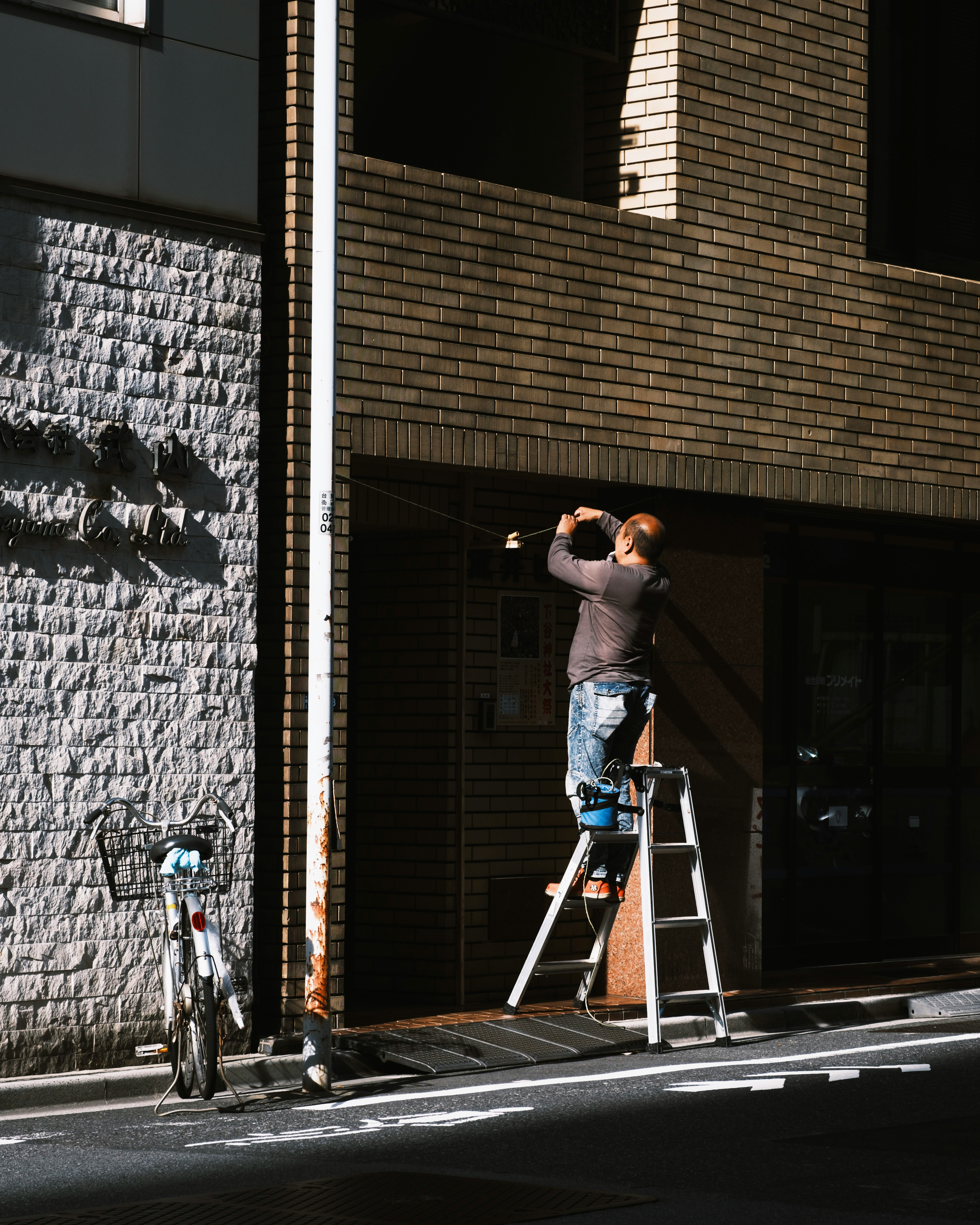 person working on a ladder in a narrow alley by a brick wall
