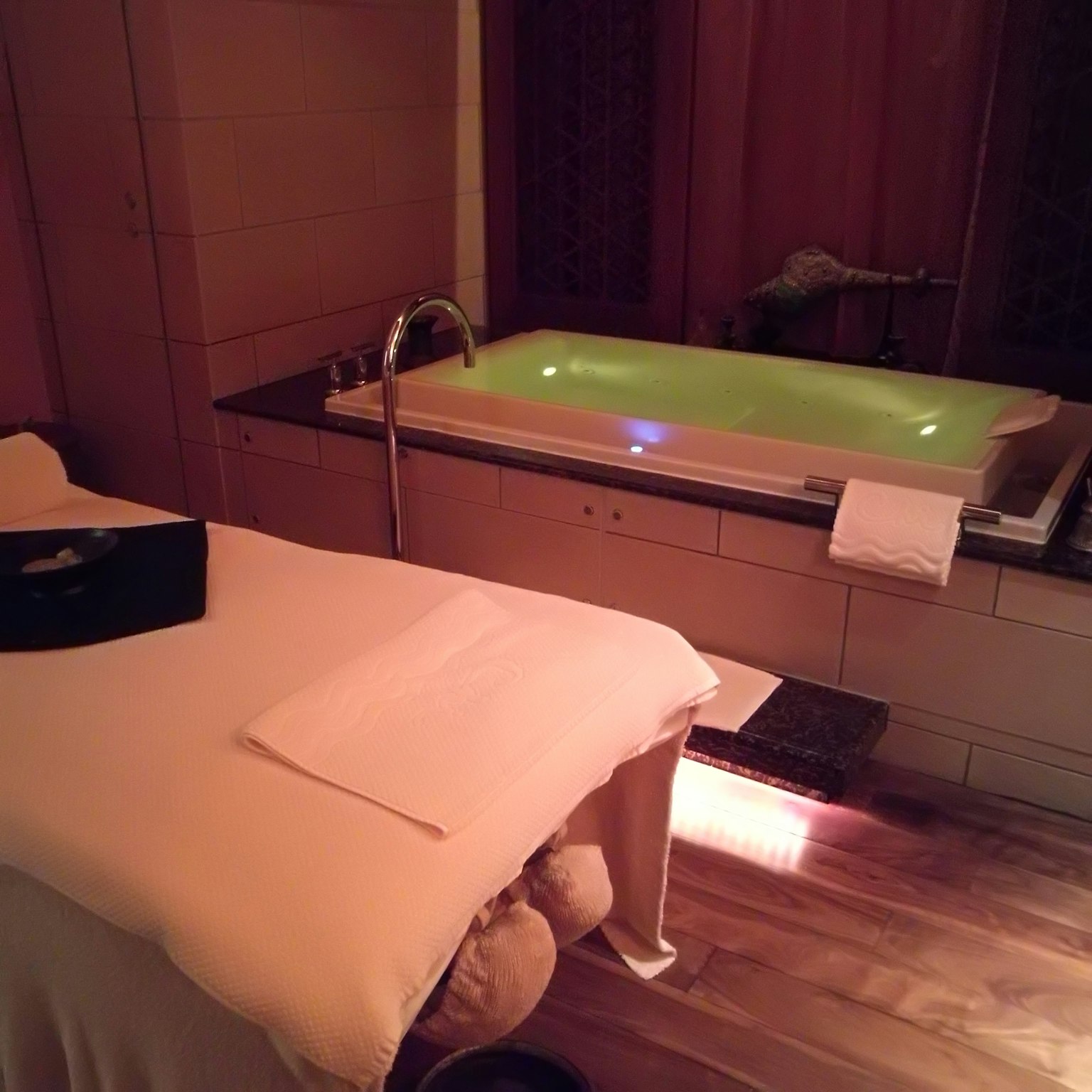 Sala de spa relajante con cama de masaje y bañera iluminada con luz verde
