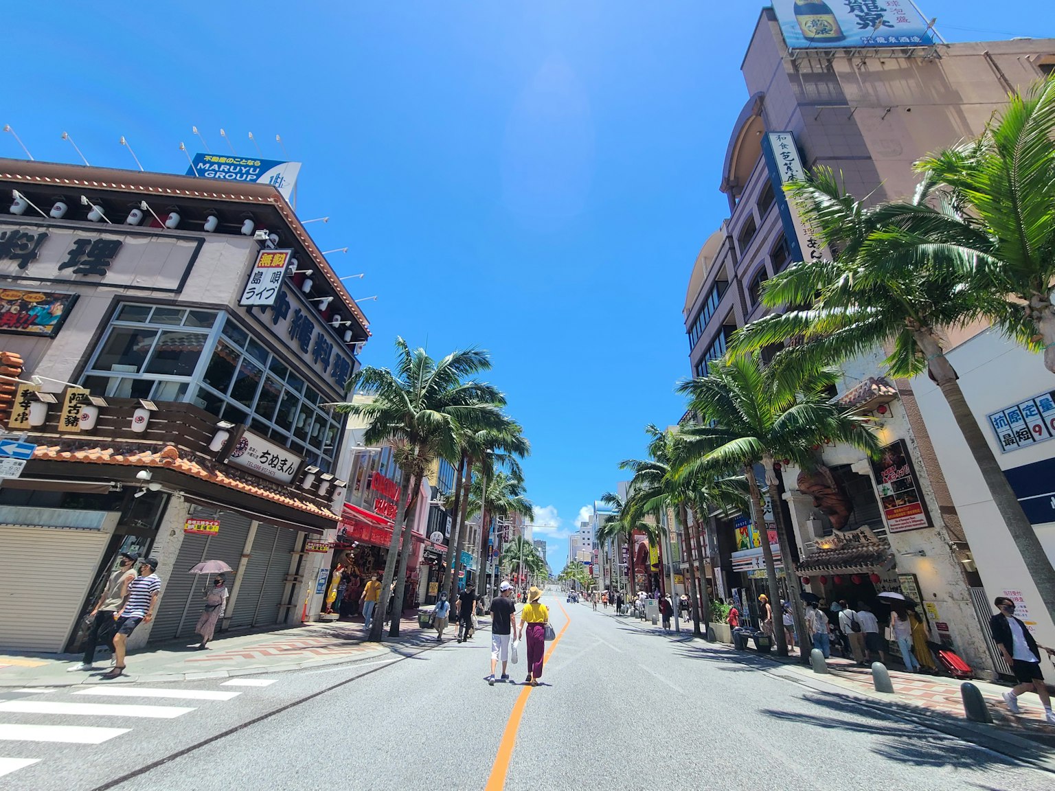 Street lined with palm trees and commercial buildings under a blue sky