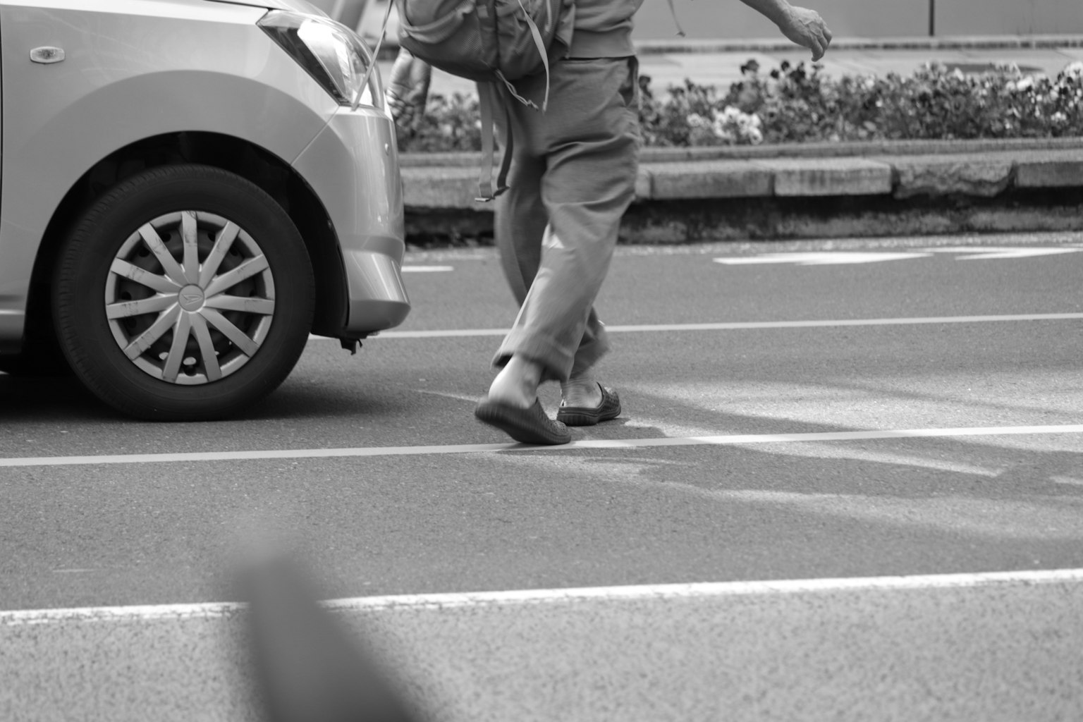 黑白畫面中一人正在過馬路靠近汽車