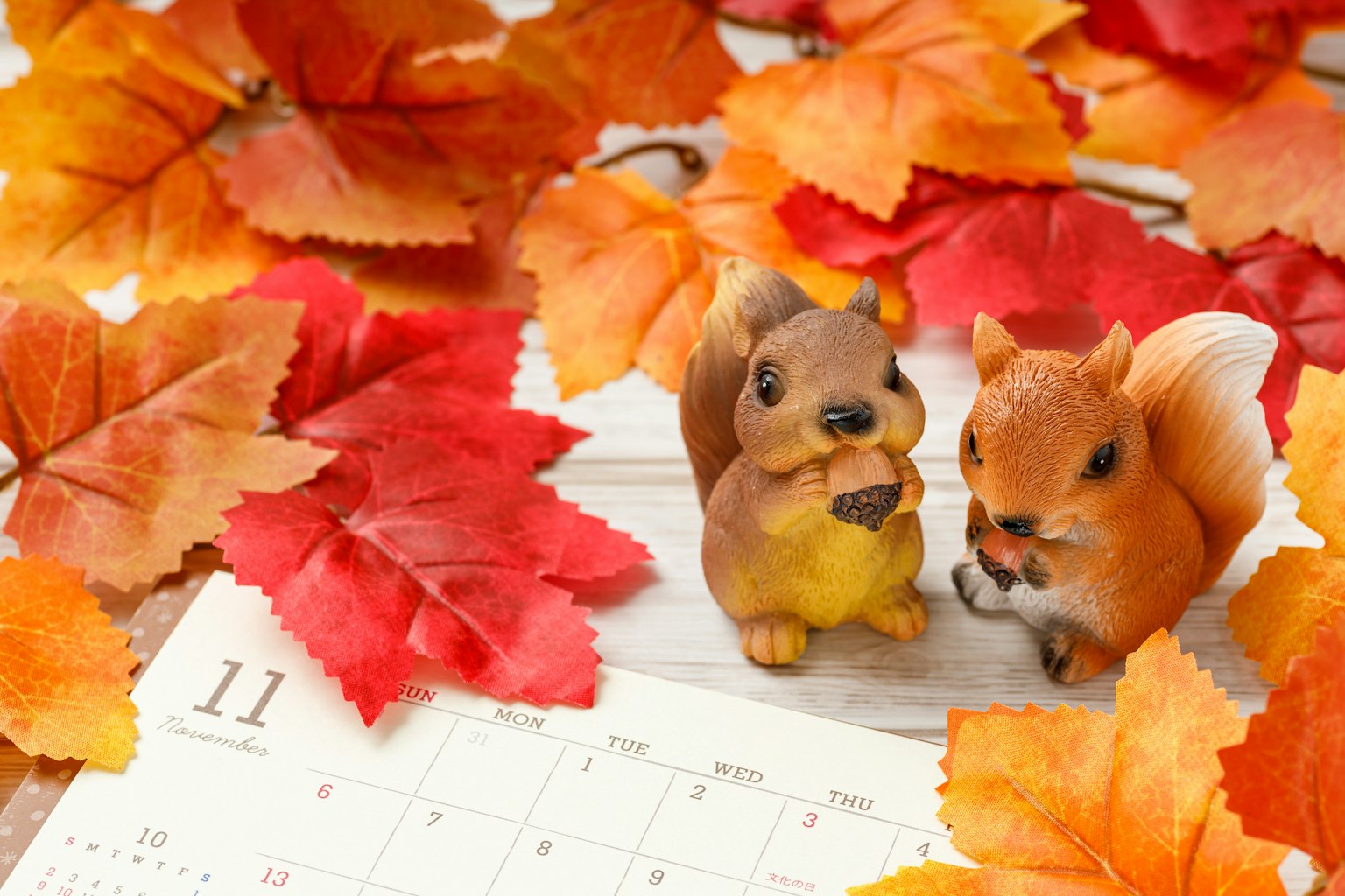 Zwei Eichhörnchen-Figuren zwischen Herbstblättern mit einem Kalender