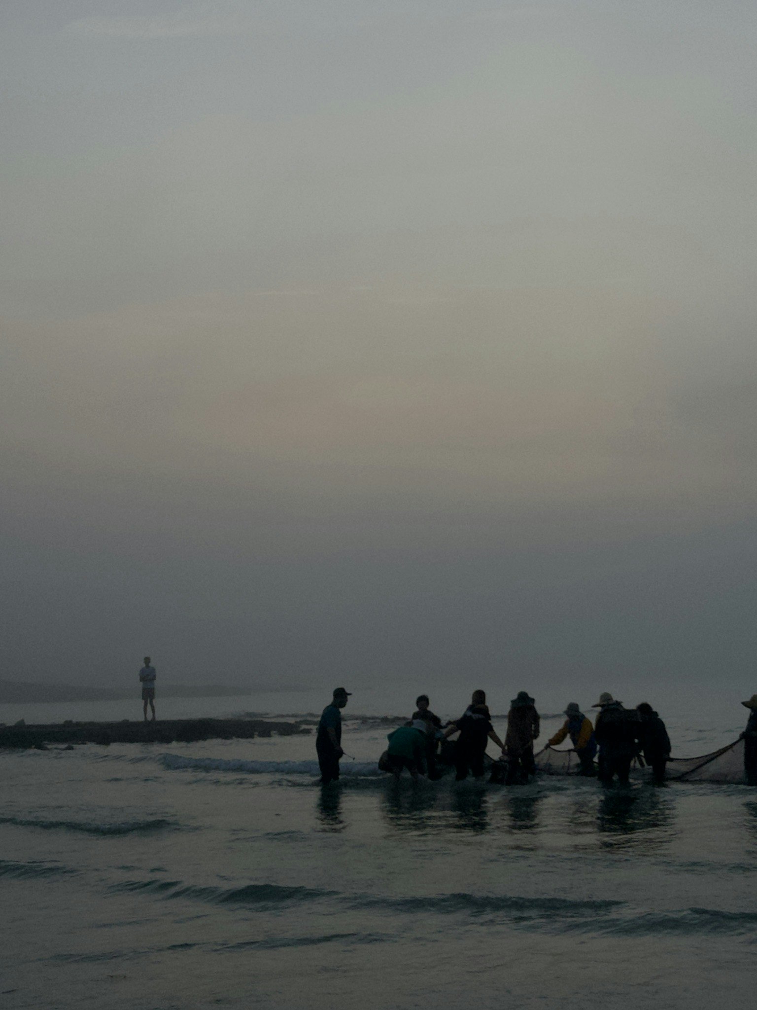 ผู้คนยืนริมชายหาดช่วงพลบค่ำ