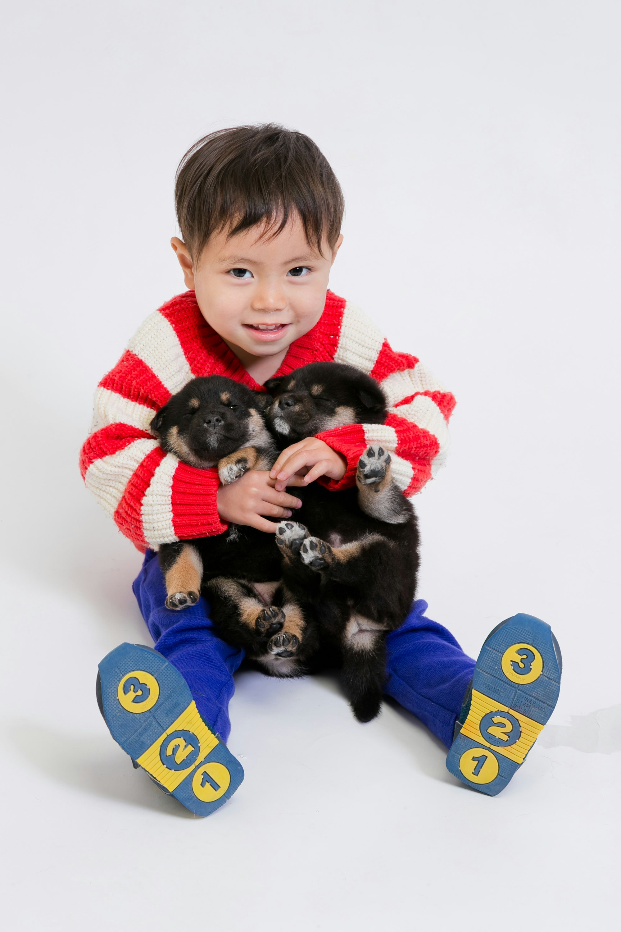 Child in red striped sweater holding black puppies