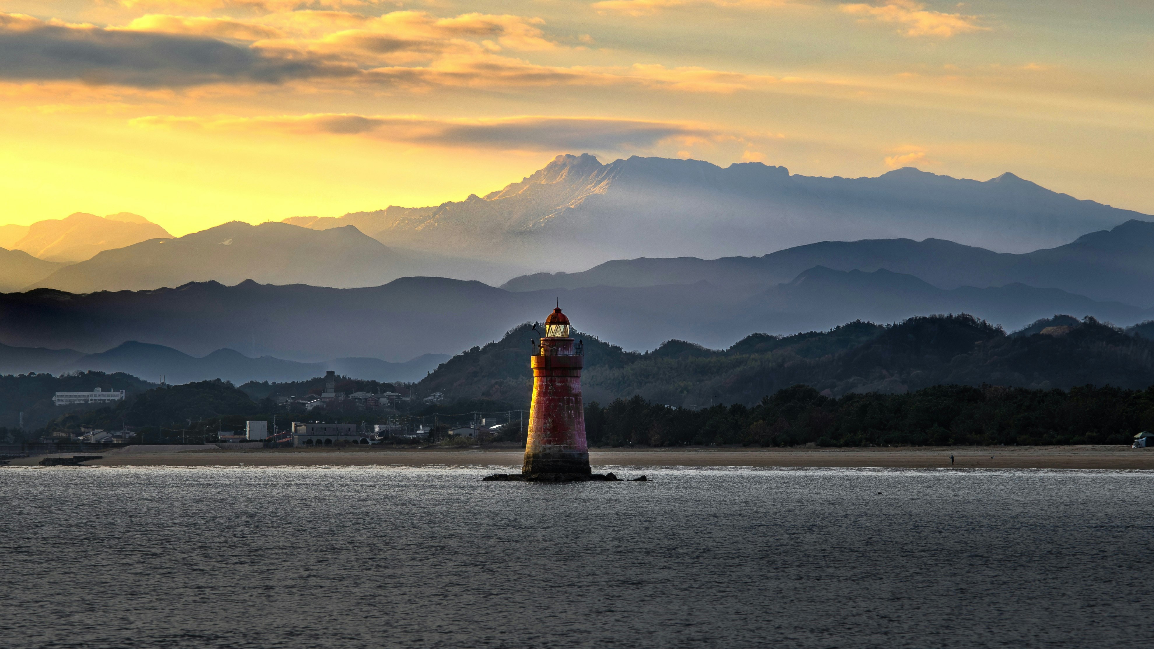 夕暮れの海上に浮かぶ灯台と山並みの風景