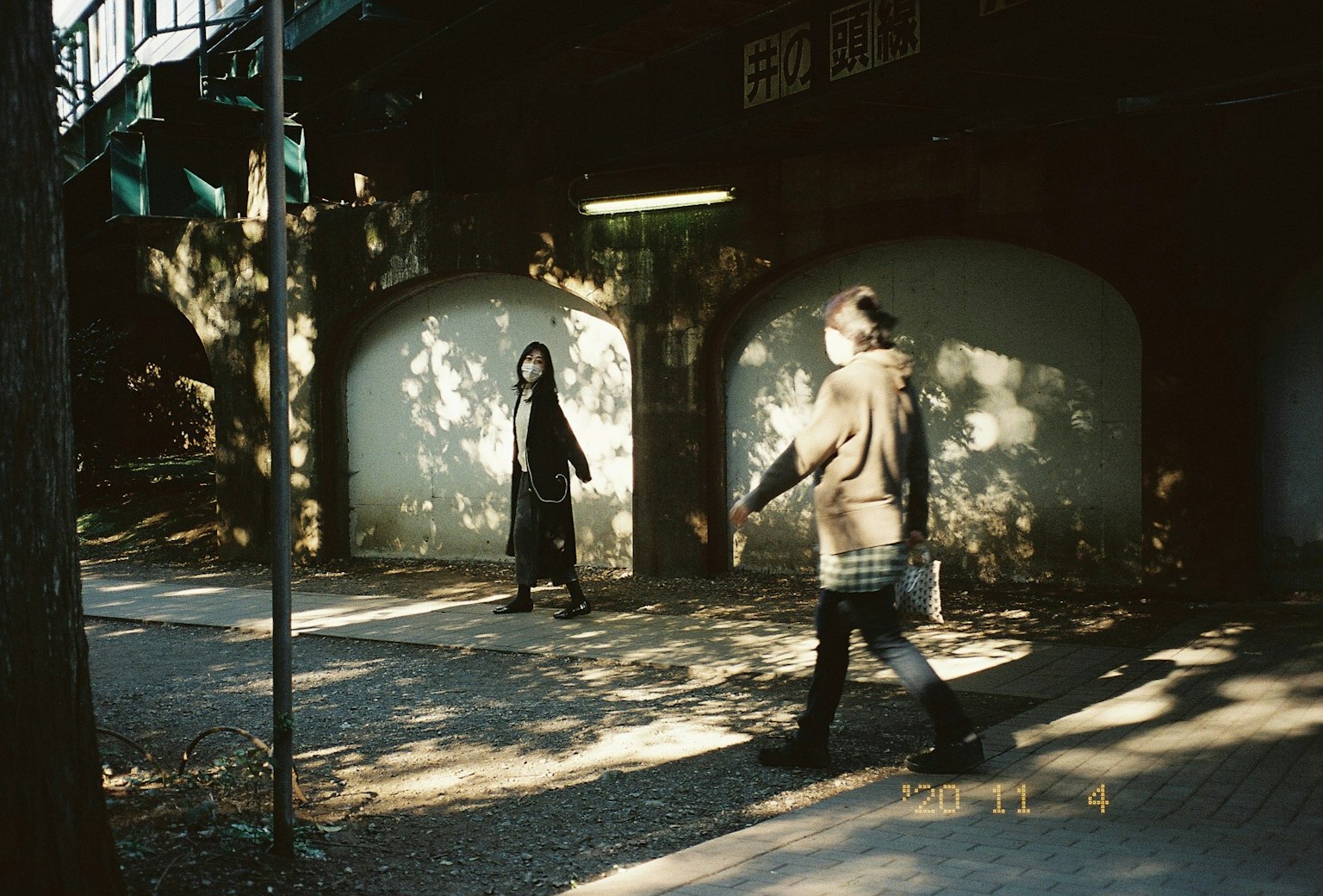 Due figure che camminano su un sentiero nel parco con forti contrasti di luce e ombra