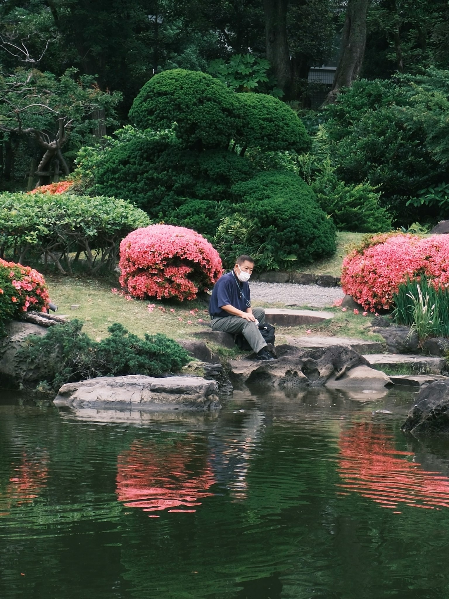 美しい庭園の池のそばに座っている人と色とりどりの花々
