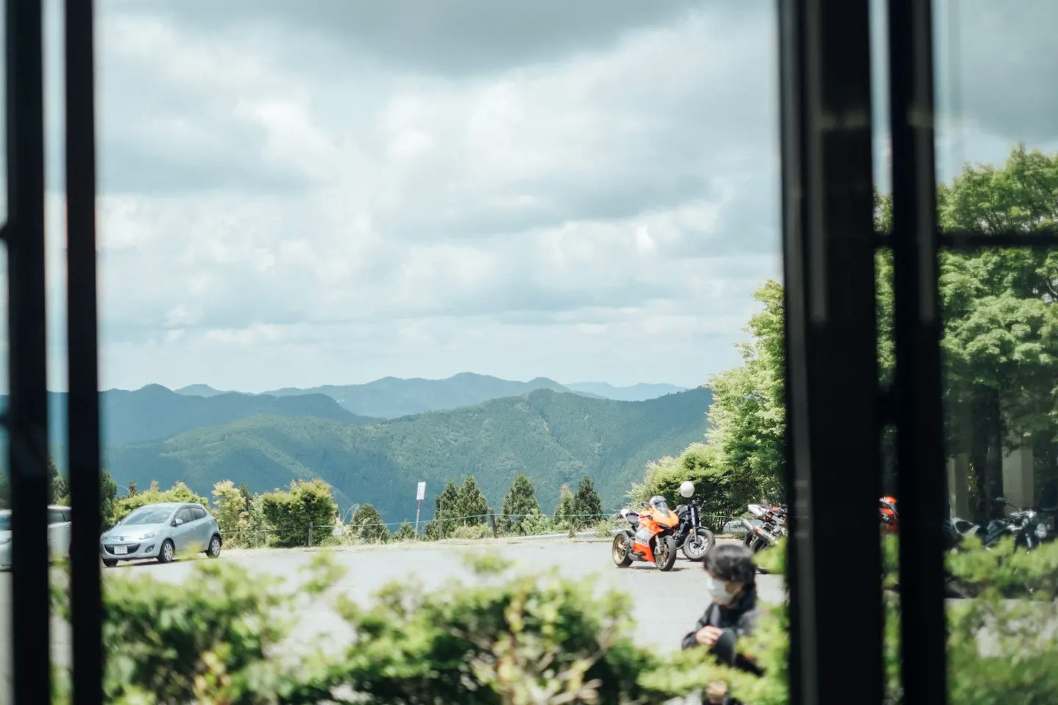 Vista di montagne e nuvole da una finestra con auto e motociclette parcheggiate