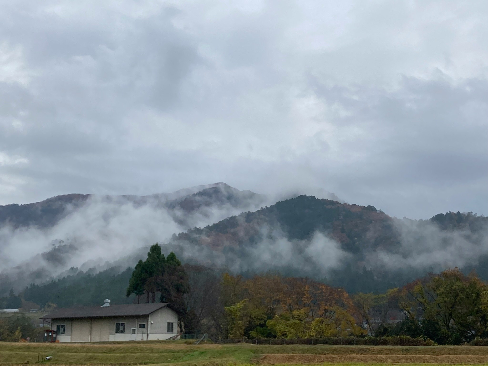 Paysage rural avec une maison et une chaîne de montagnes dans la brume