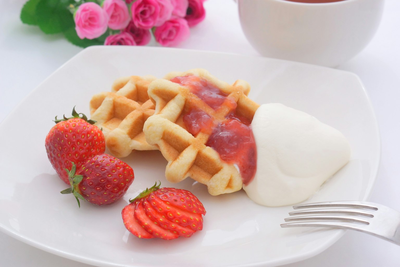 Wafles cubiertos con salsa de fresa y crema servidos con fresas frescas