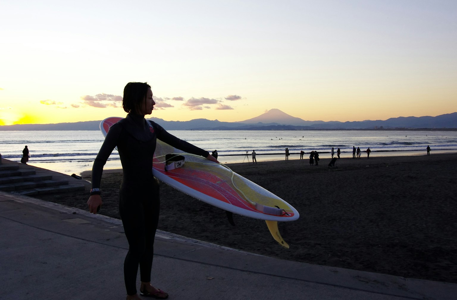 Donna che tiene una tavola da surf contro il tramonto con una montagna sullo sfondo