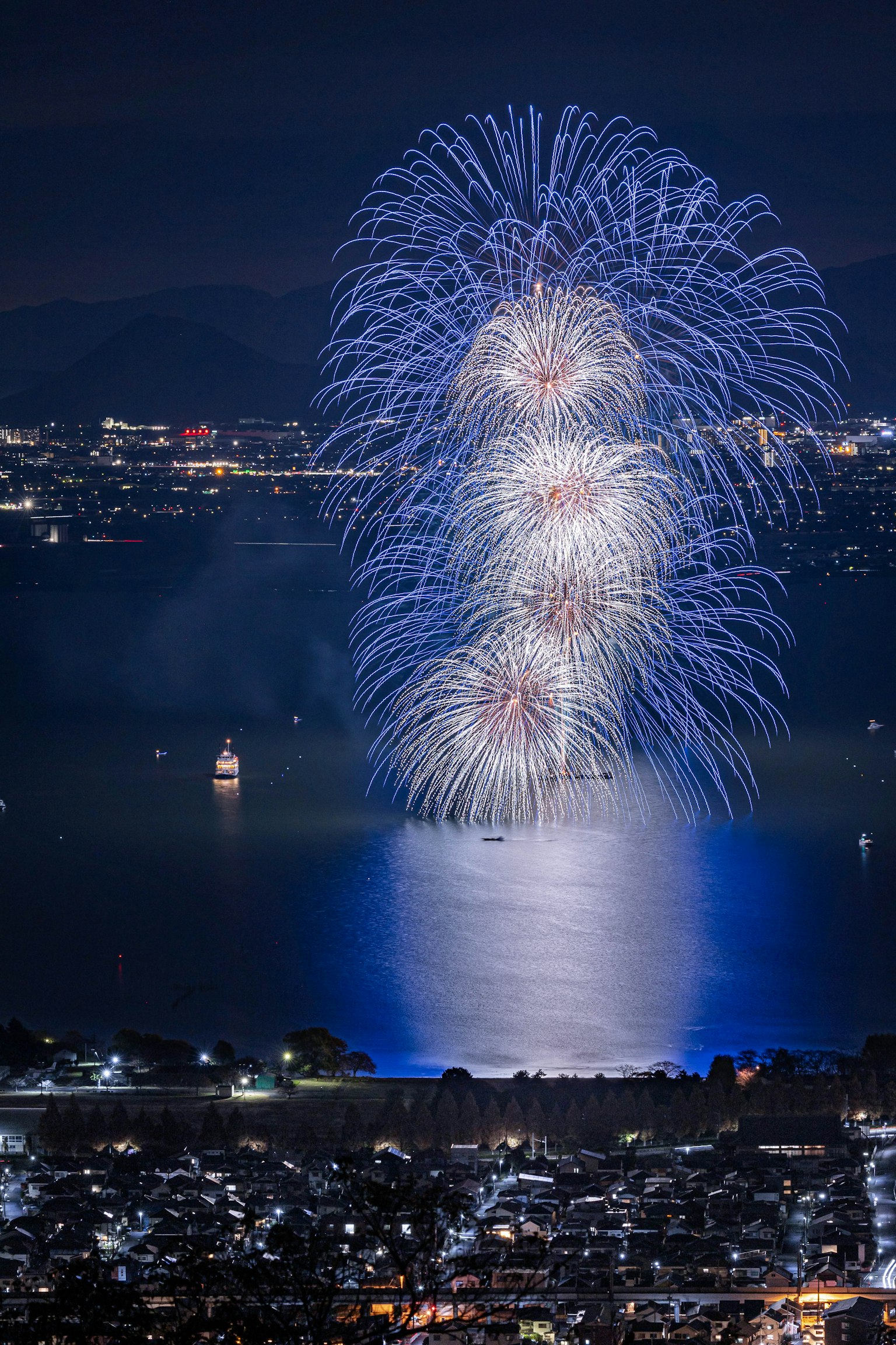 Hermoso espectáculo de fuegos artificiales azules reflejándose en el lago por la noche
