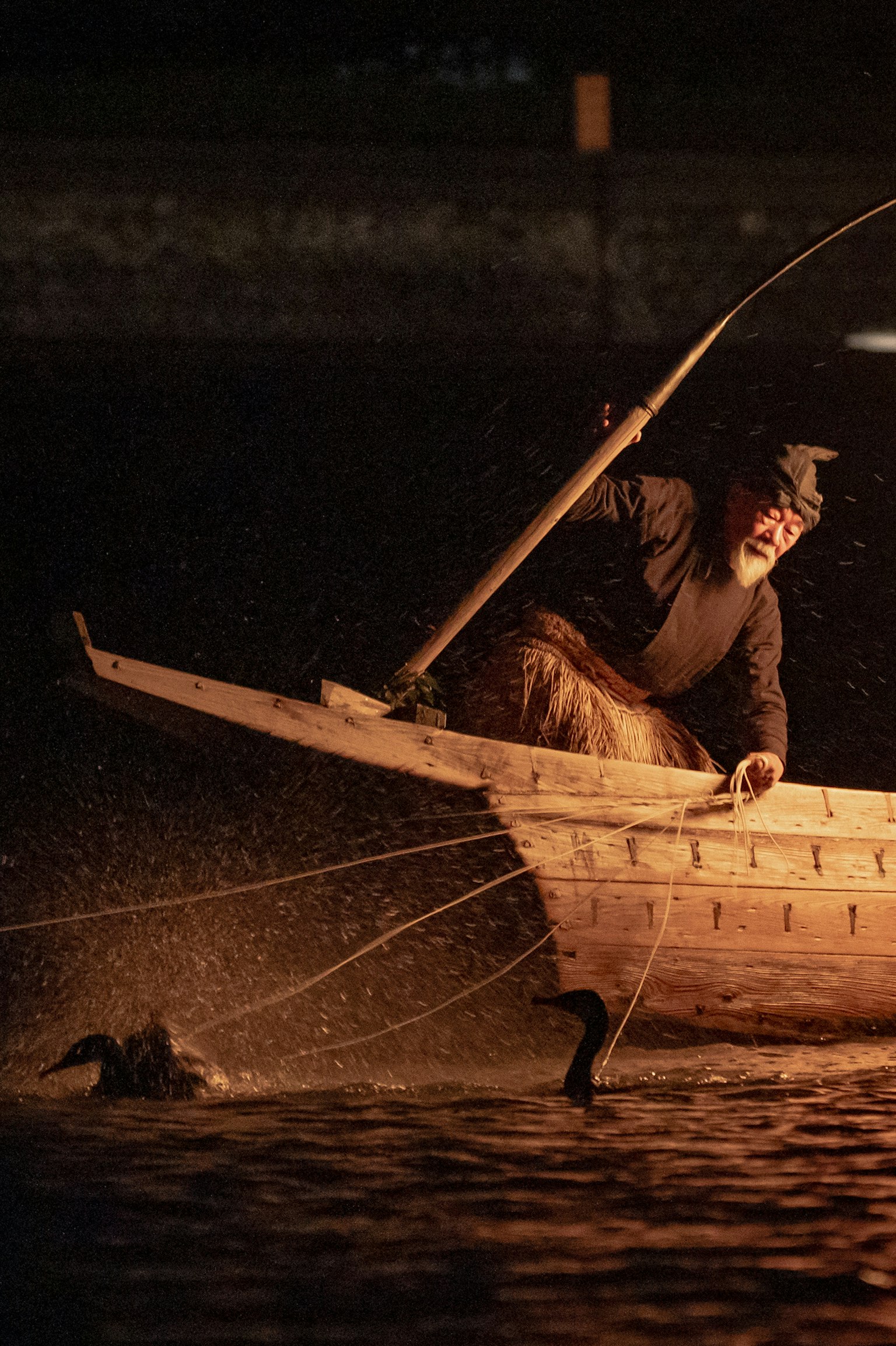 A fisherman trying to catch ducks on the water at night in a traditional boat