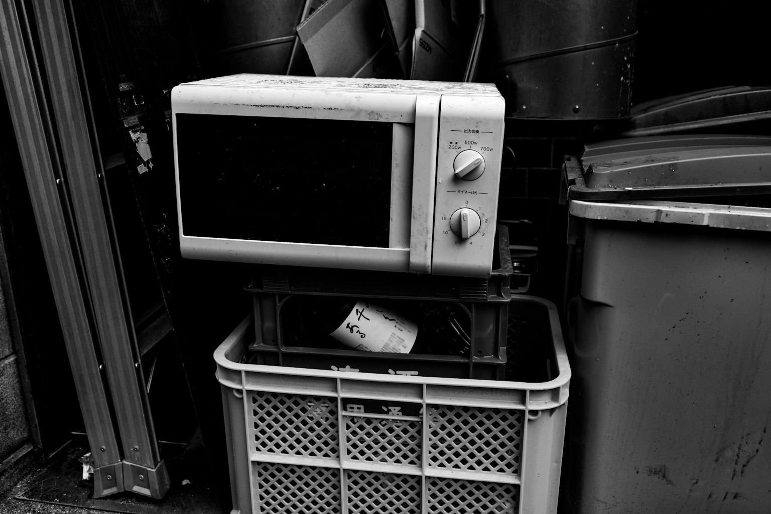 Old microwave placed amidst trash bins and a basket