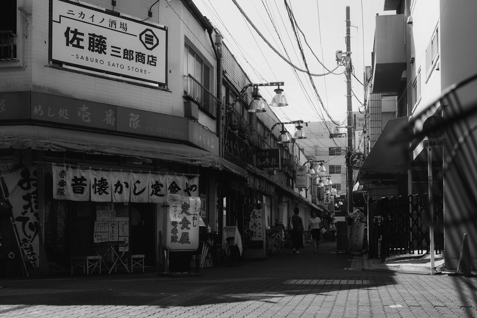 Escena de calle en blanco y negro con letreros de tiendas y líneas eléctricas