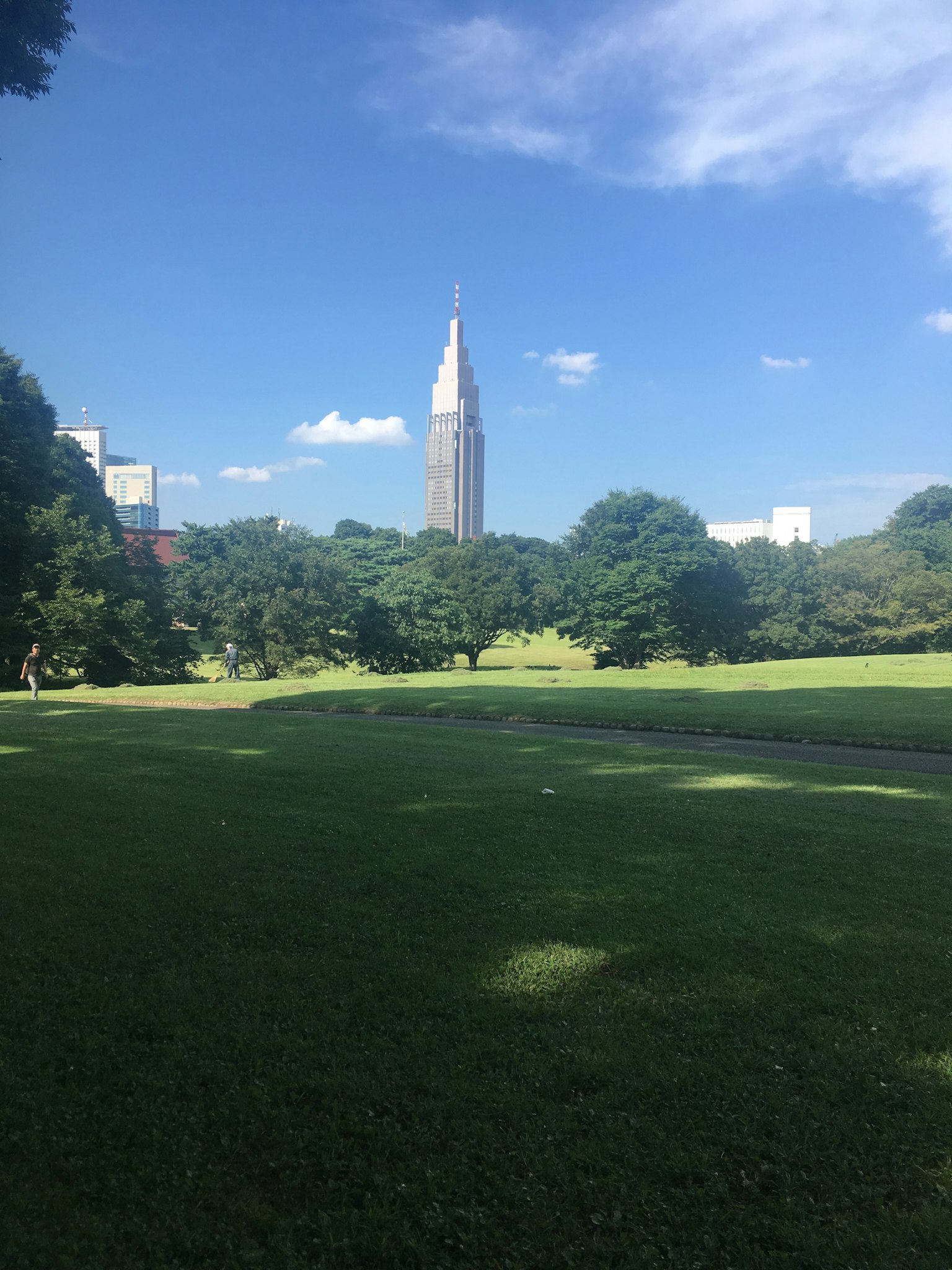 Gedung pencakar langit tinggi di bawah langit biru dengan taman hijau