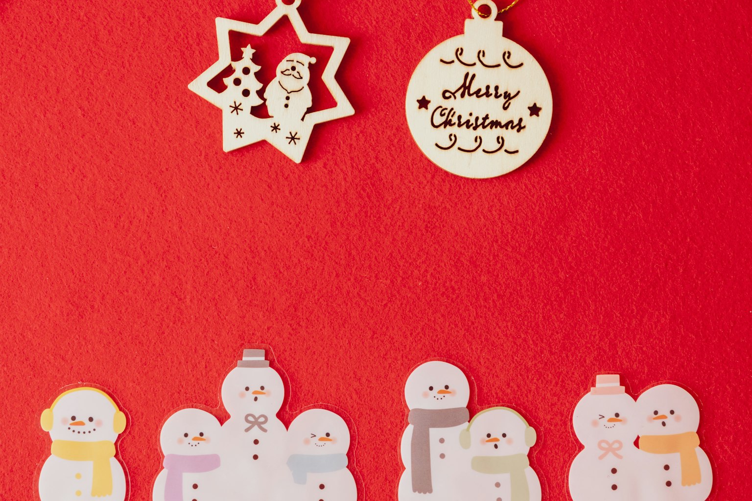 Decoraciones navideñas con recortes de muñecos de nieve y un adorno de madera sobre un fondo rojo