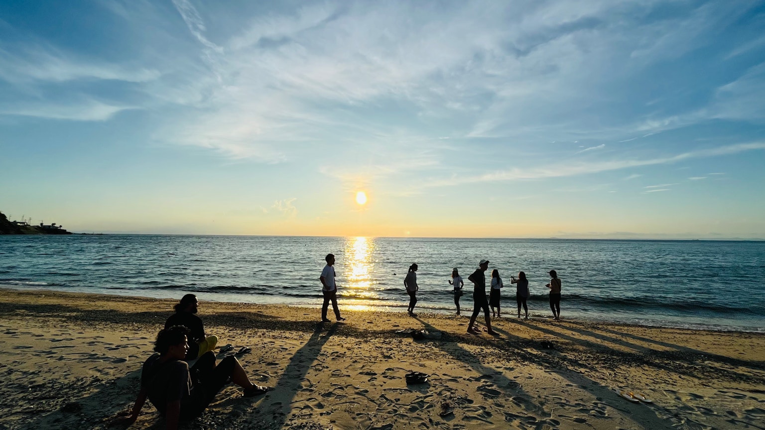 Siluetas de personas jugando en la playa con un atardecer de fondo
