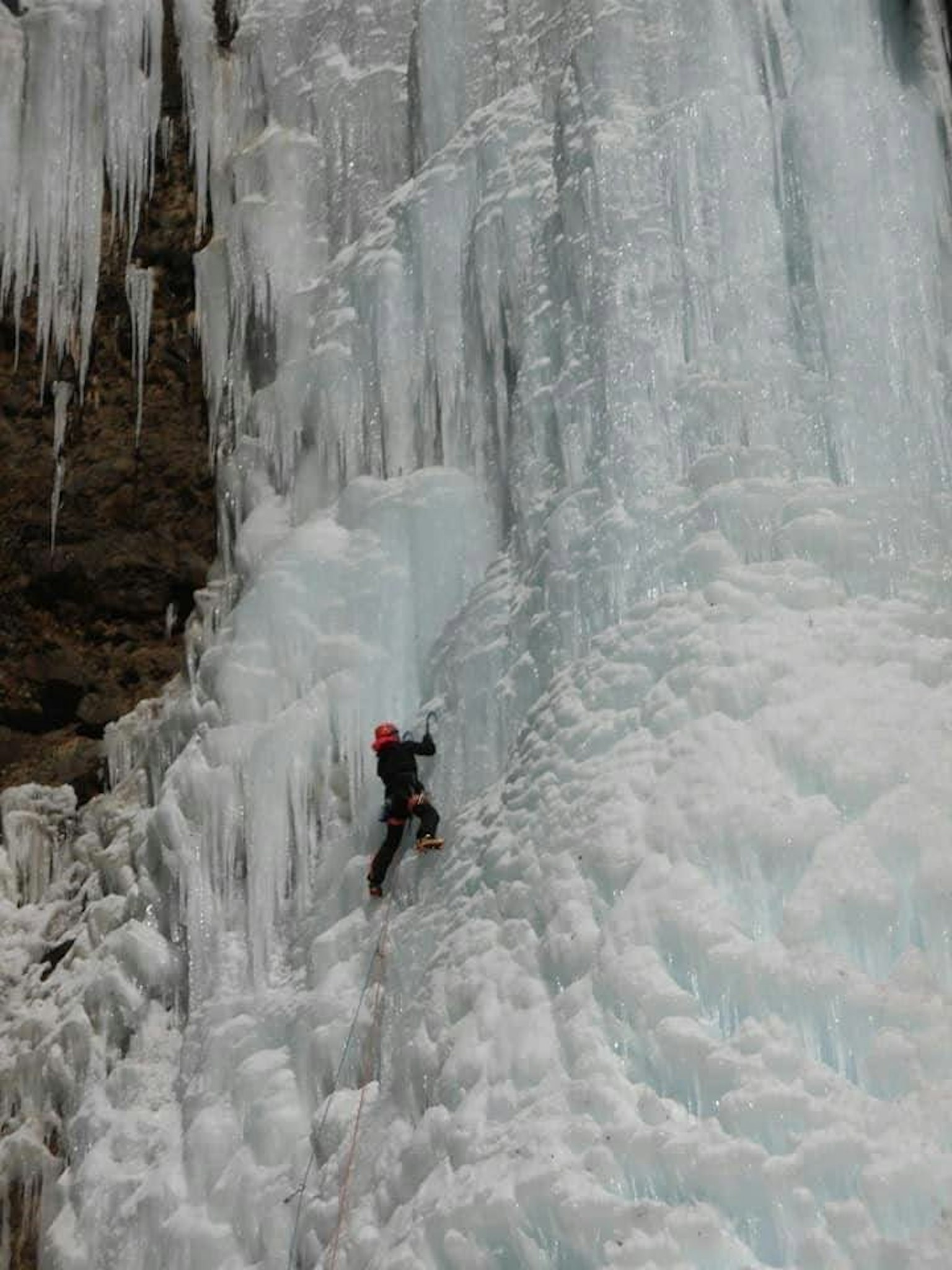 Grimpeur montant une cascade de glace portant un casque rouge
