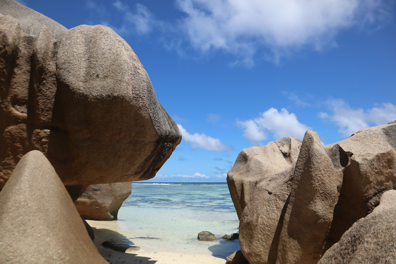 ทิวทัศน์ชายหาดที่มีหินขนาดใหญ่ล้อมรอบด้วยท้องฟ้าและทะเลสีฟ้า