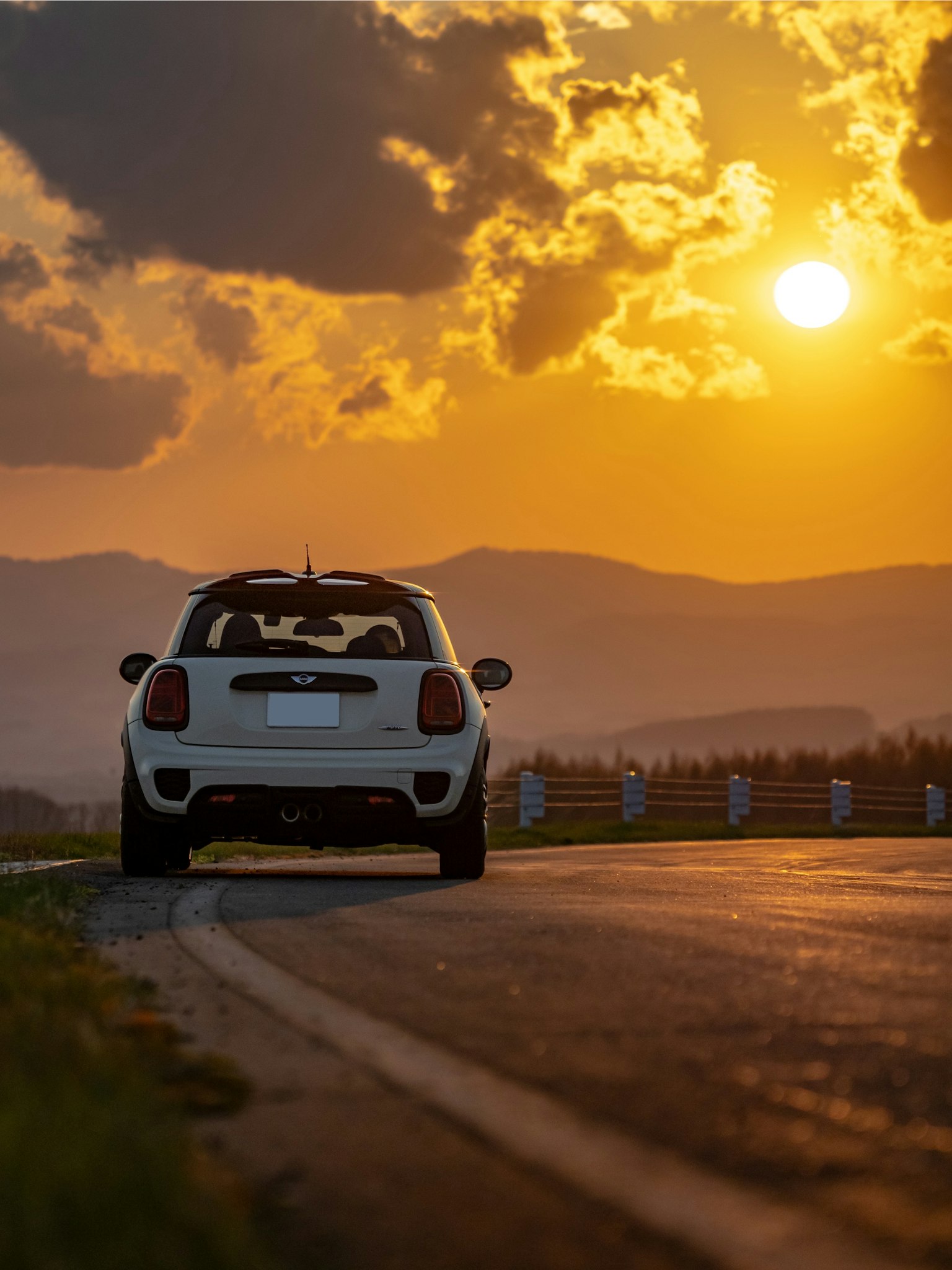 Ein weißes Auto, das auf der Straße mit einem Sonnenuntergang im Hintergrund geparkt ist