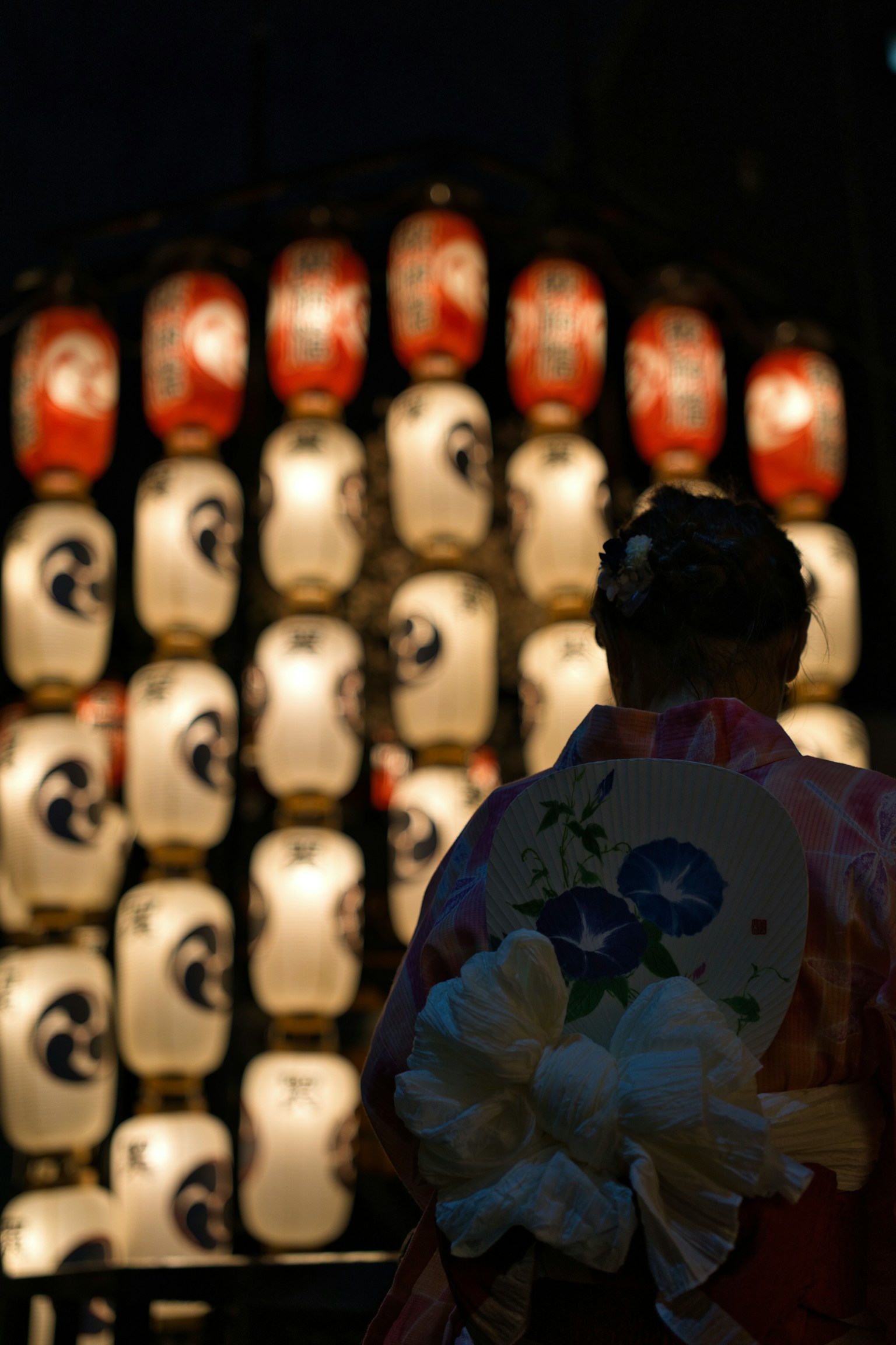 A woman in a kimono standing in front of lanterns during a festival at night