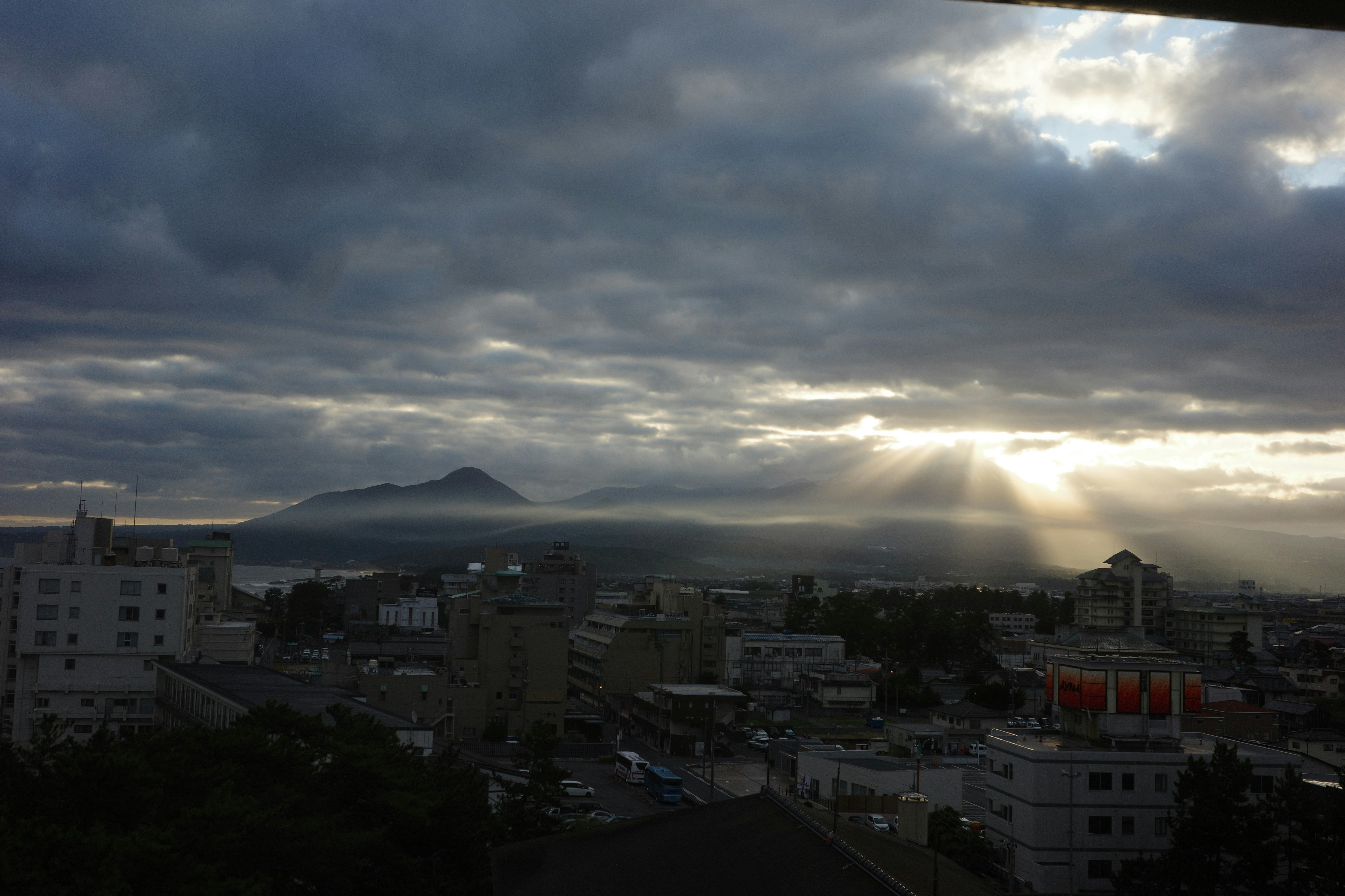 View of a town skyline with sunlight breaking through clouds and Mount Daisen