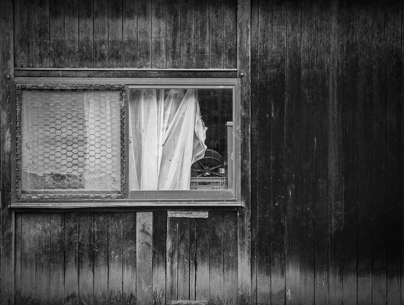 Ventana antigua con cortina blanca en una pared de madera negra