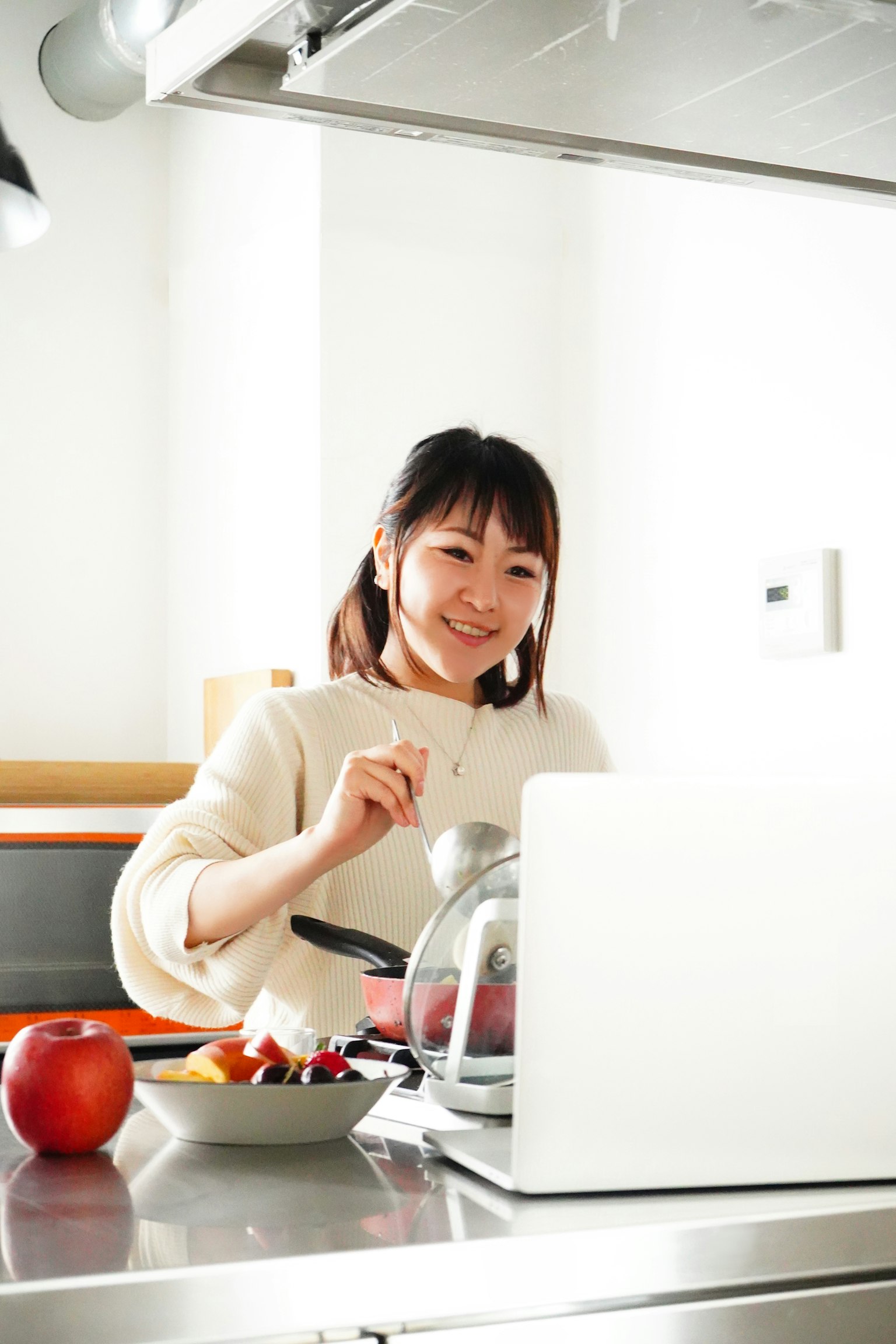 Wanita tersenyum menyiapkan makanan di dapur dengan laptop