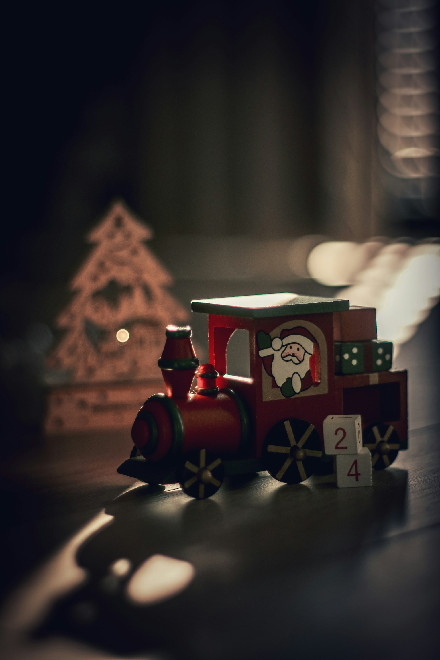 Sebuah kereta mainan merah dengan Santa dan pohon Natal kayu dalam suasana redup