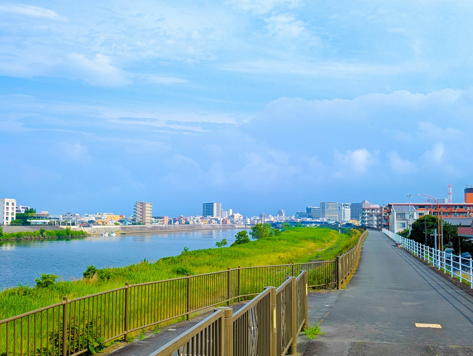 ทางเดินริมน้ำที่สวยงามพร้อมหญ้าสีเขียวใต้ท้องฟ้าสีฟ้า