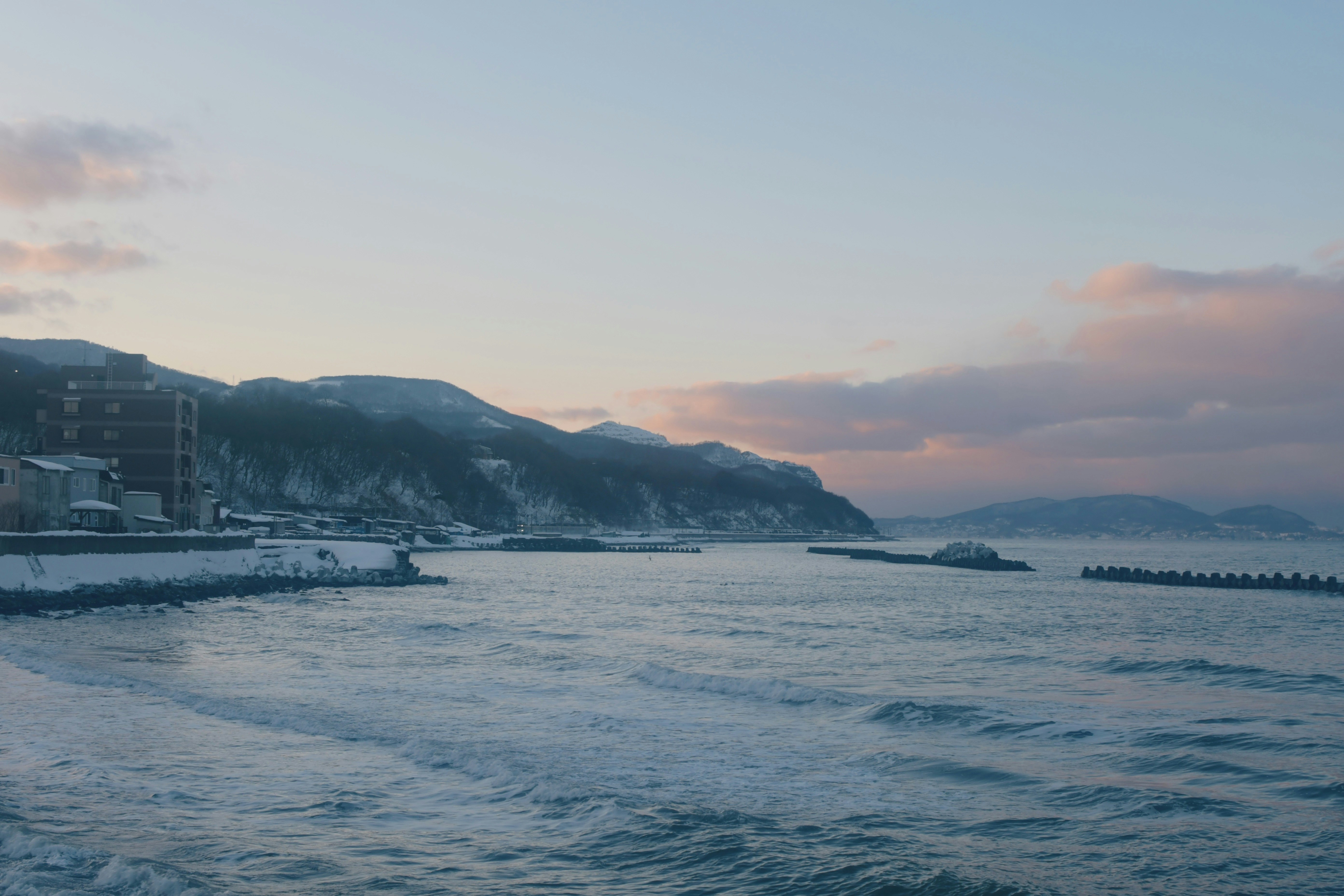夕暮れの海沿いを走る波と遠くの岬の風景