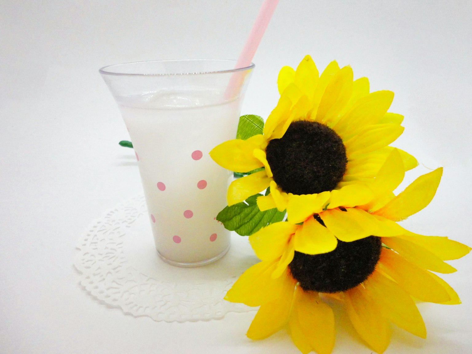 Un bicchiere trasparente con una cannuccia rosa riempito di una bevanda bianca accanto a girasoli gialli