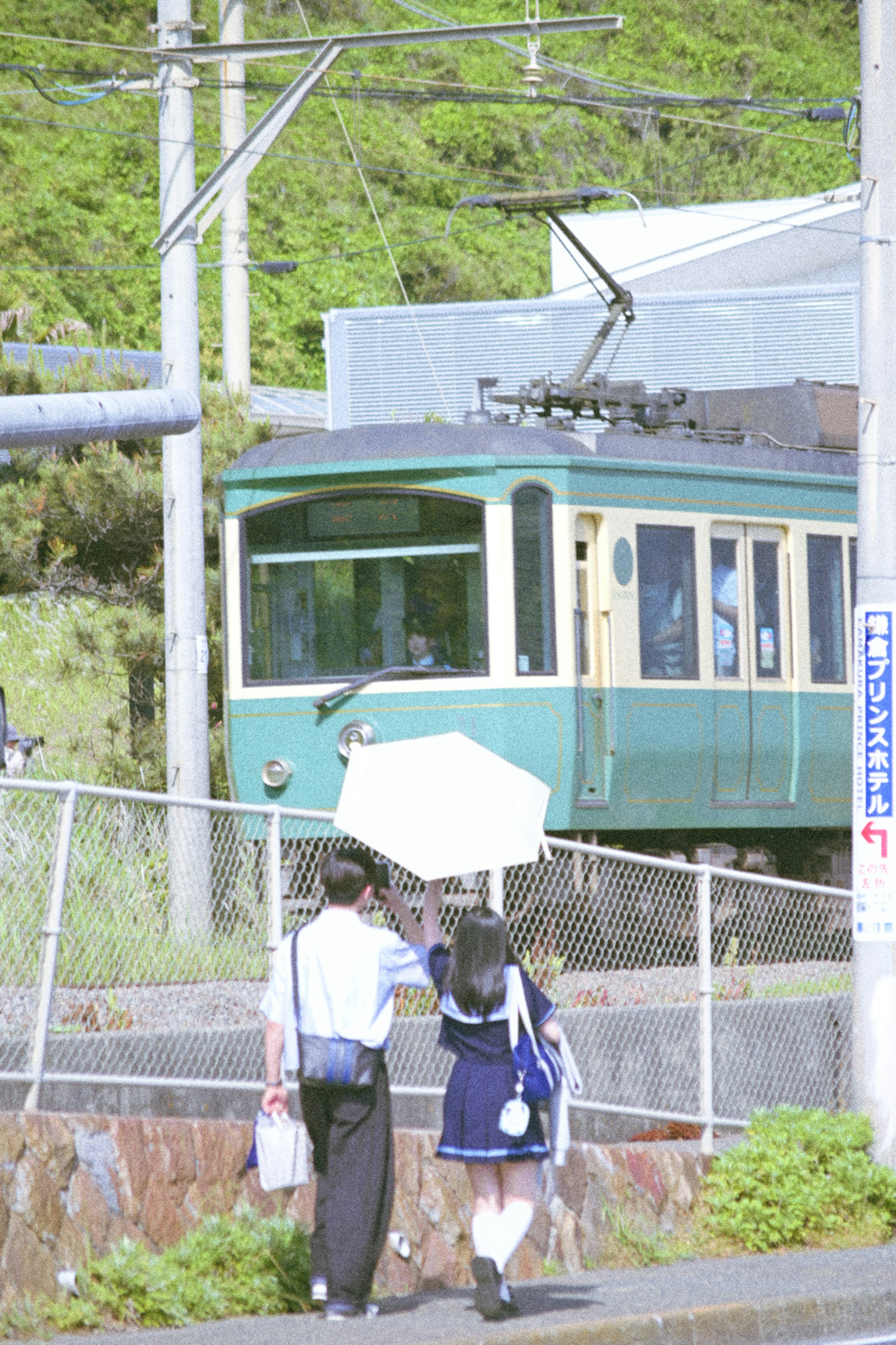 線路沿いを歩く人と緑の車両が見える鉄道風景
