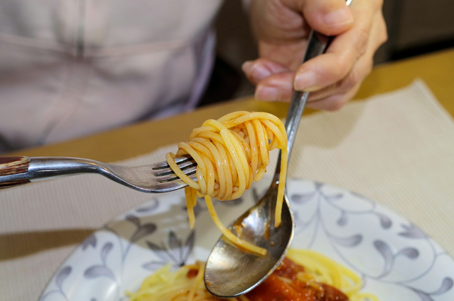 A hand twirling spaghetti with a fork and spoon