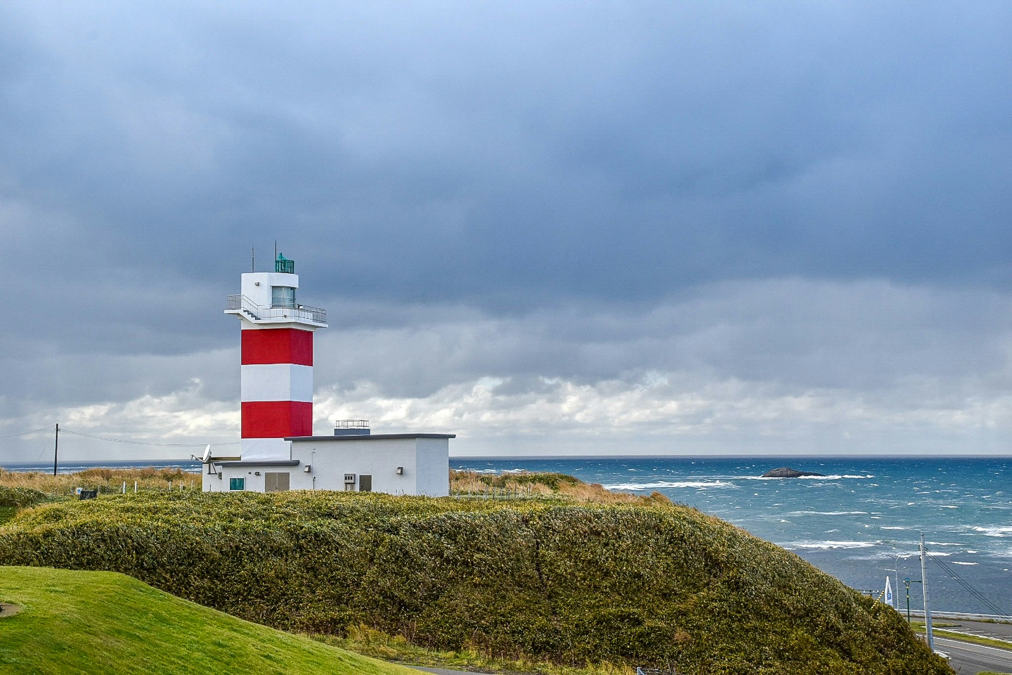 phare sur une colline côtière couverte d’herbe sous un ciel nuageux